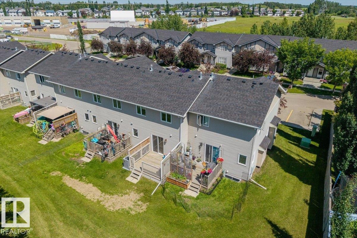 Rear exterior of a townhouse featuring light gray siding and dark shingle roofing - 125 Birchwood Close, Devon, AB