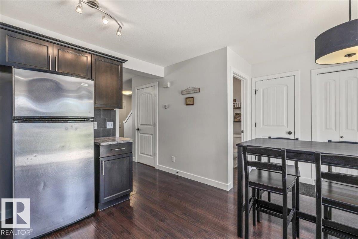 Kitchen area featuring dark wood-finish flooring, dark cabinetry, and a stainless steel refrigerator - 125 Birchwood Close, Devon, AB