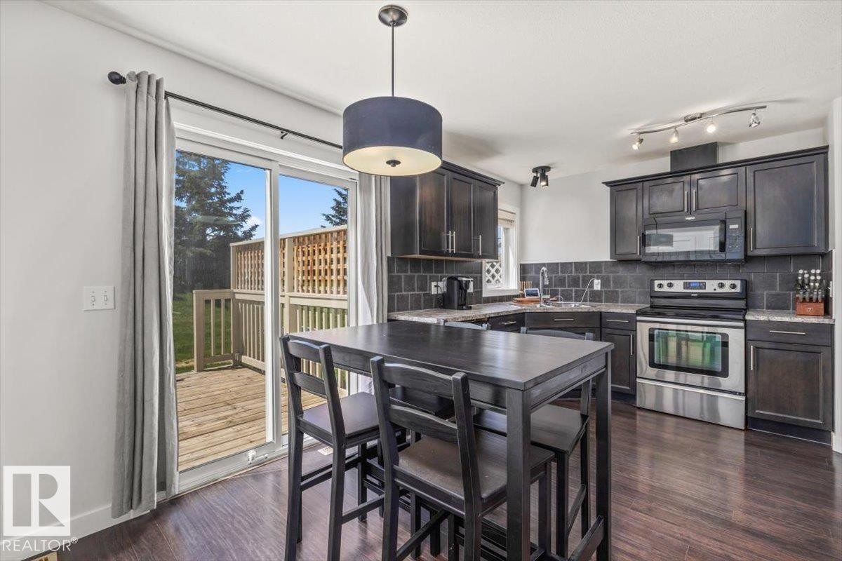 Contemporary kitchen featuring dark wood cabinetry, stainless steel appliances, and a tiled backsplash - 125 Birchwood Close, Devon, AB