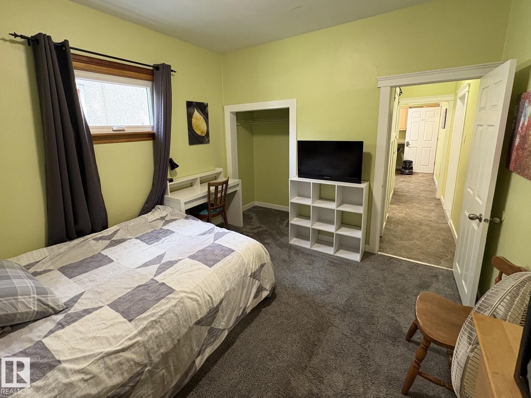 Carpeted room featuring a built-in desk, window with wood trim, and an open doorway revealing a hallway with patterned flooring - 11511 101 Street, Edmonton, AB