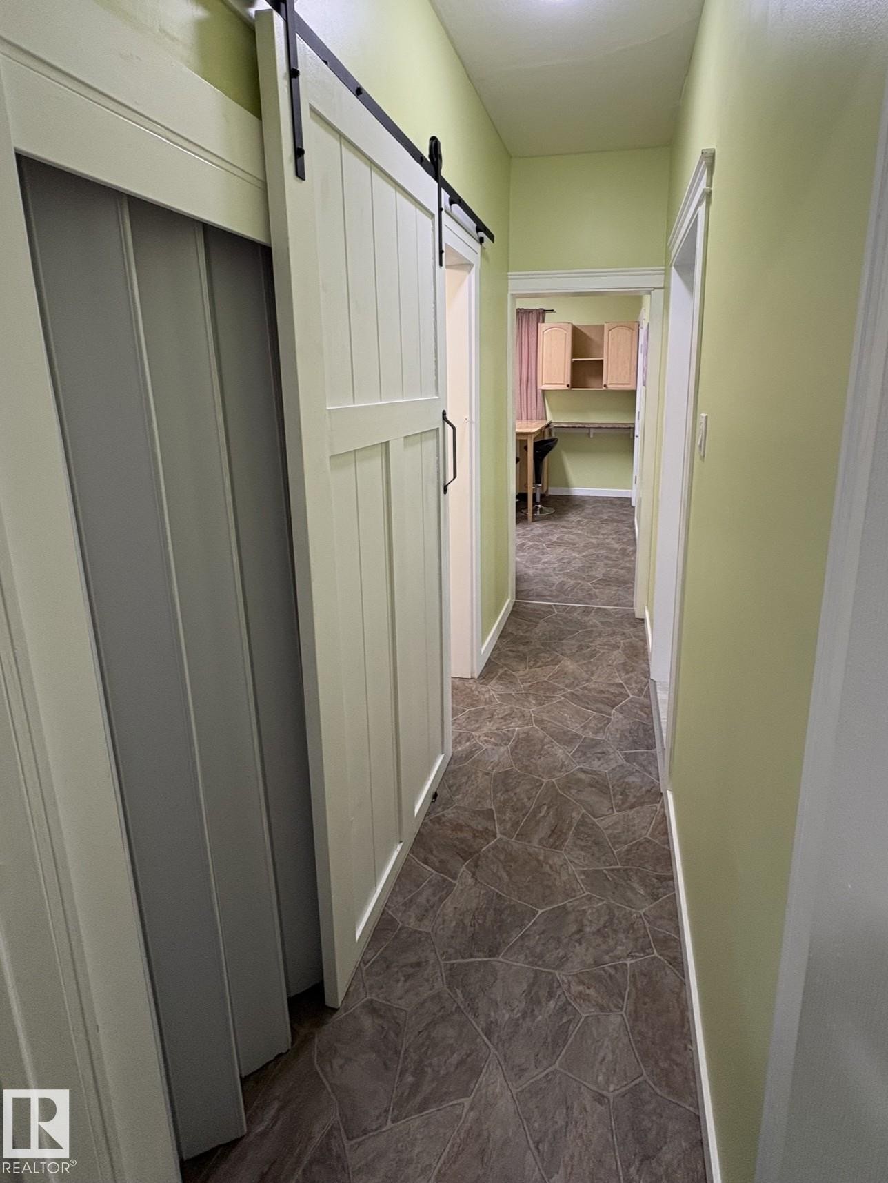 Hallway featuring a white barn door with black hardware, neutral tile flooring, and light green walls - 11511 101 Street, Edmonton, AB