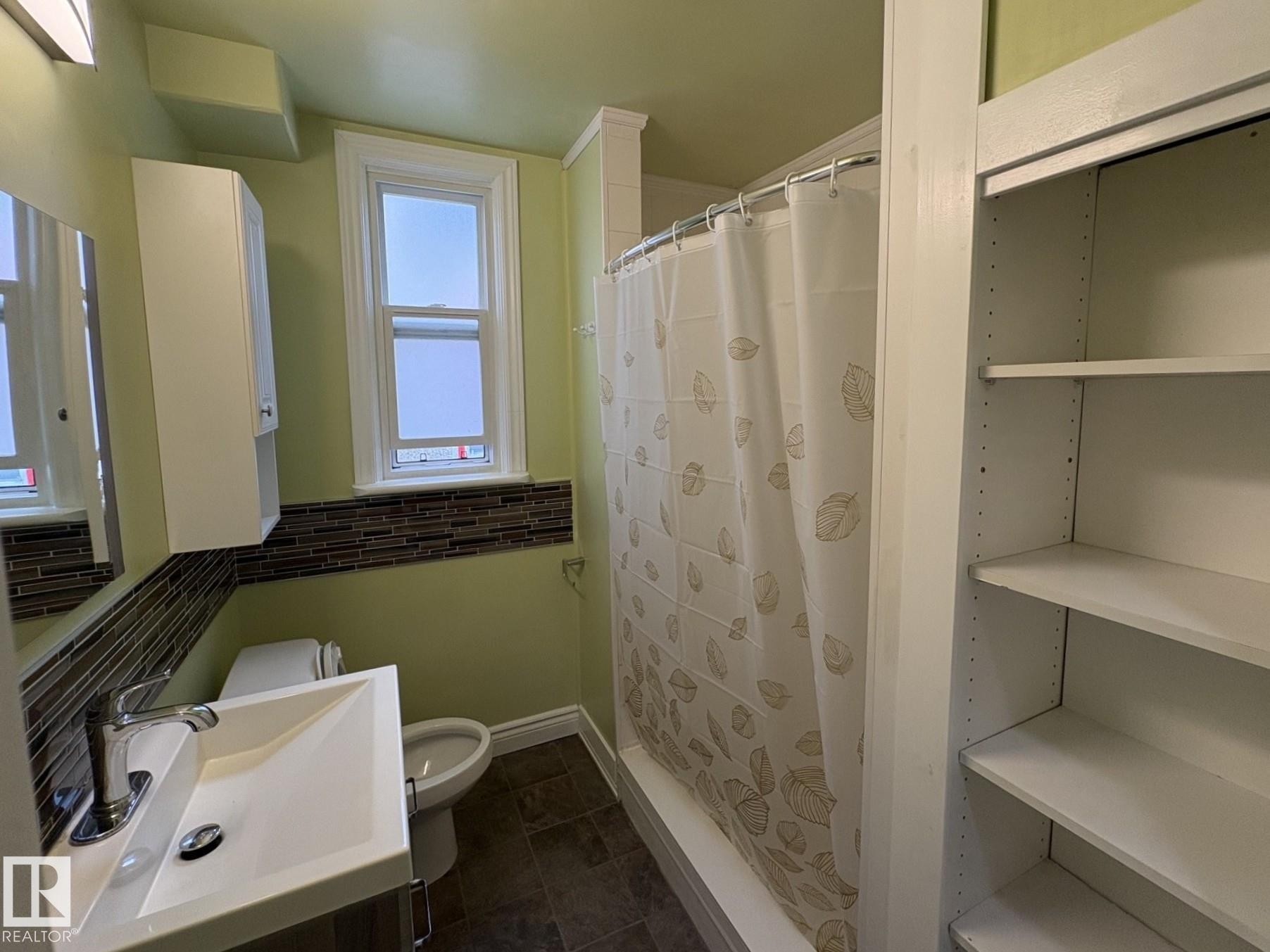 Bathroom featuring a single window, a tile-surround bathtub with shower, a vanity sink with chrome hardware, and built-in shelving - 11511 101 Street, Edmonton, AB