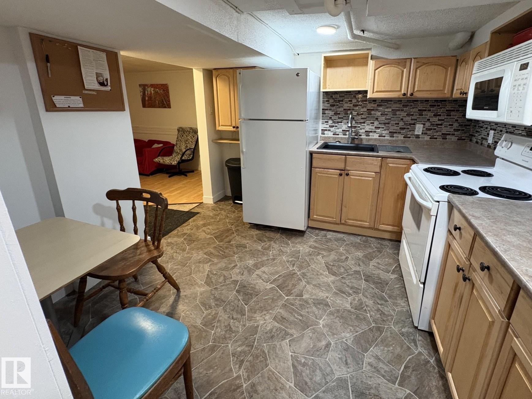 Kitchen featuring light wood cabinetry, a mosaic tile backsplash, and stone-look flooring - 11511 101 Street, Edmonton, AB