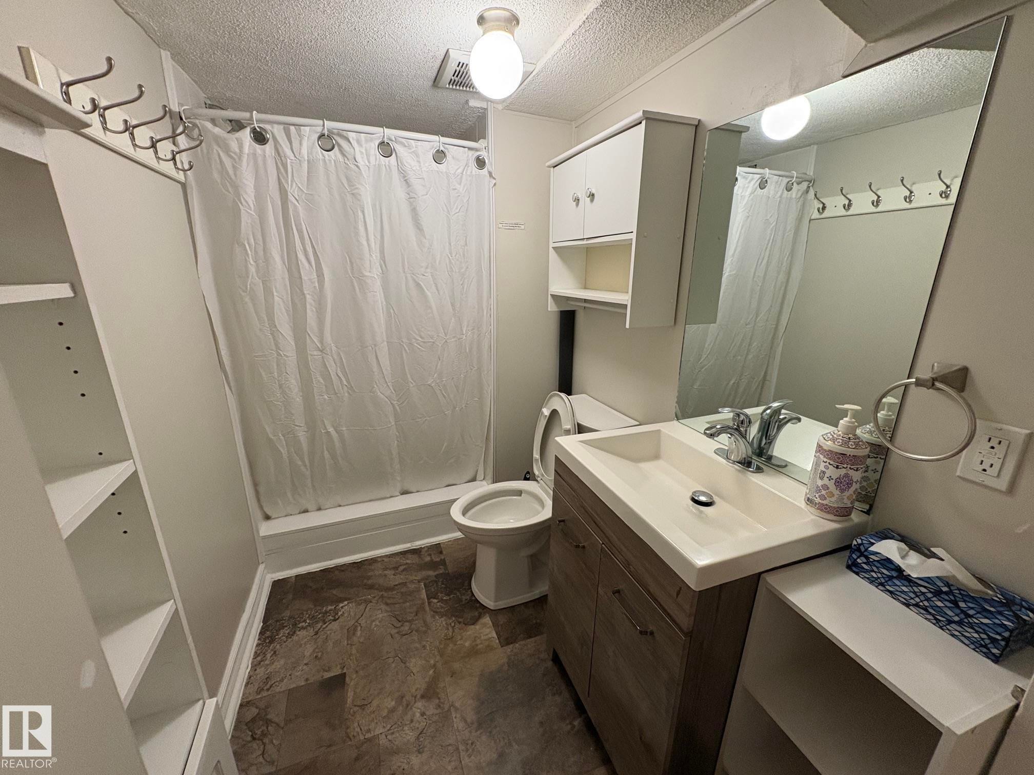 Bathroom featuring a single vanity with a rectangular sink, wood-finish cabinetry, and a large mirror - 11511 101 Street, Edmonton, AB