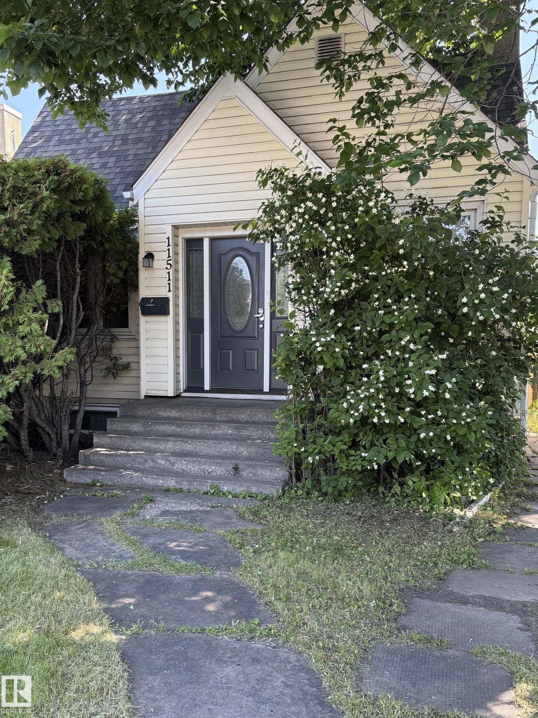 Front exterior with light-colored siding and a dark entry door featuring an oval glass insert - 11511 101 Street, Edmonton, AB