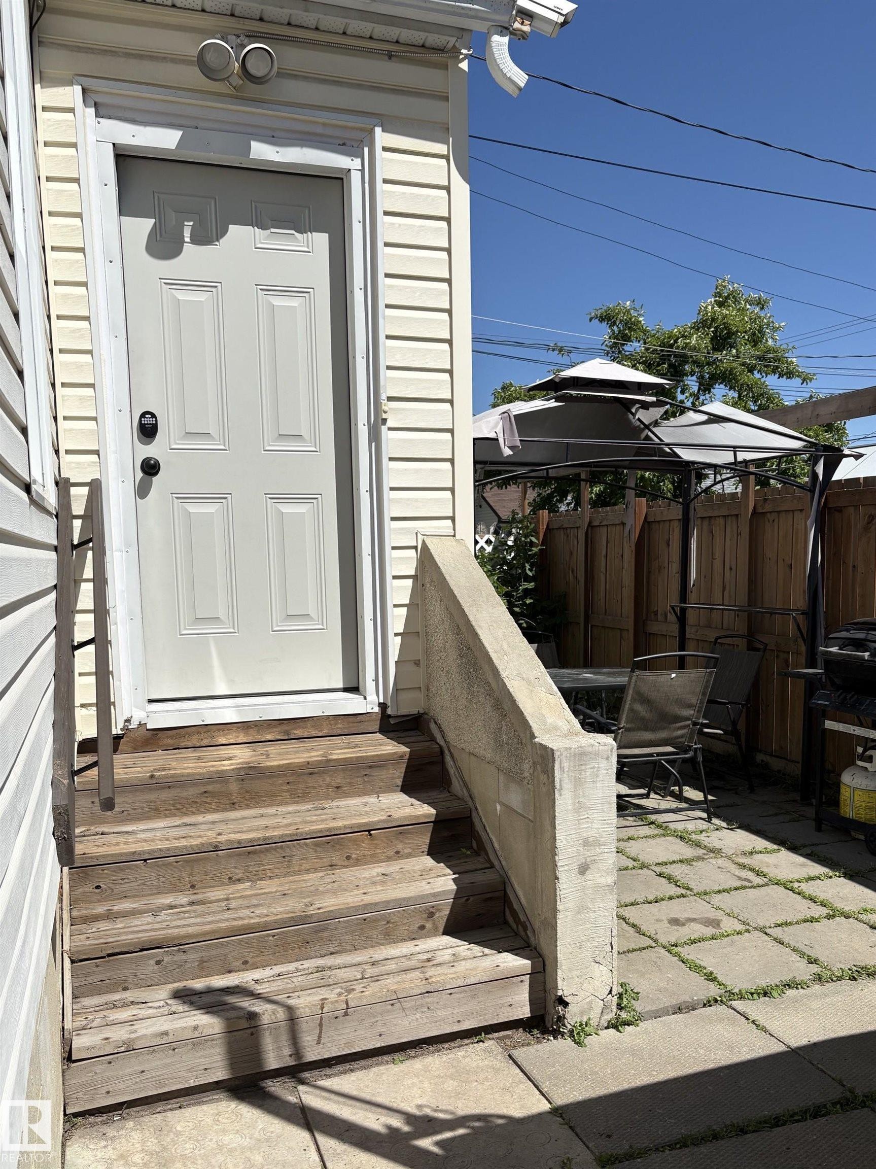Exterior door with floodlight fixture, wooden steps, and a concrete handrail - 11511 101 Street, Edmonton, AB