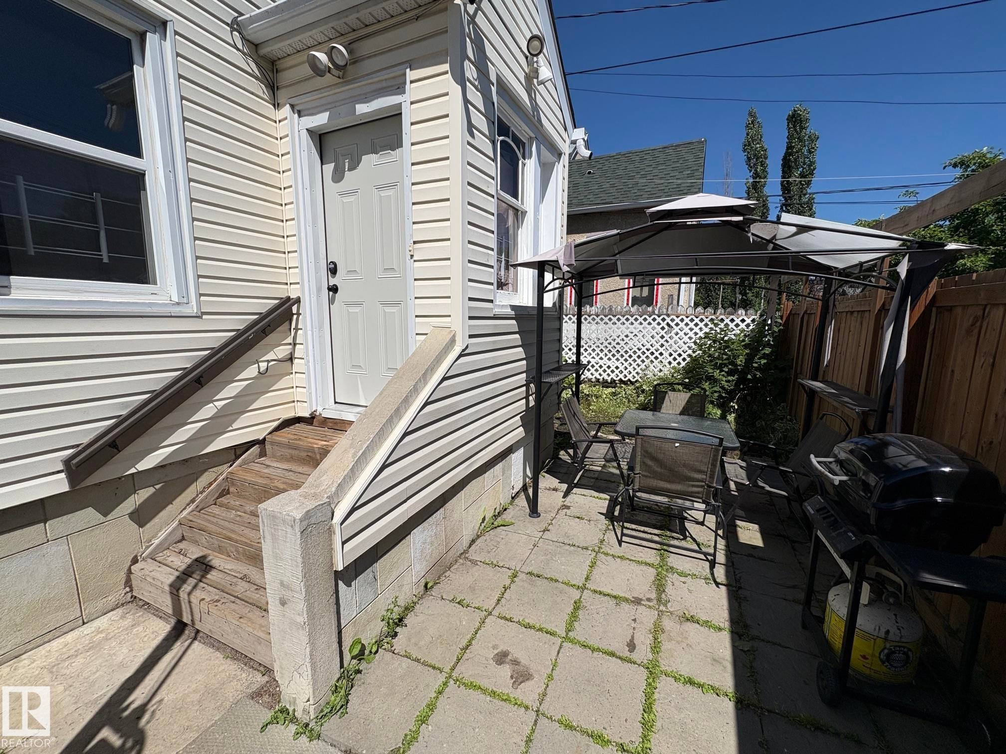 Exterior featuring horizontal vinyl siding, a white paneled door, and a concrete patio with pavers - 11511 101 Street, Edmonton, AB