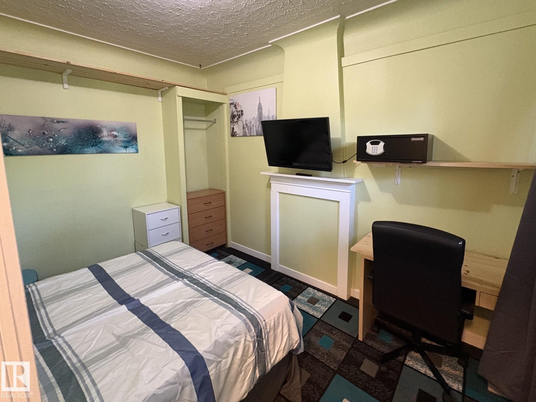 Room featuring light green walls, a patterned carpet, and a built-in closet with hanging rod and shelf - 11511 101 Street, Edmonton, AB