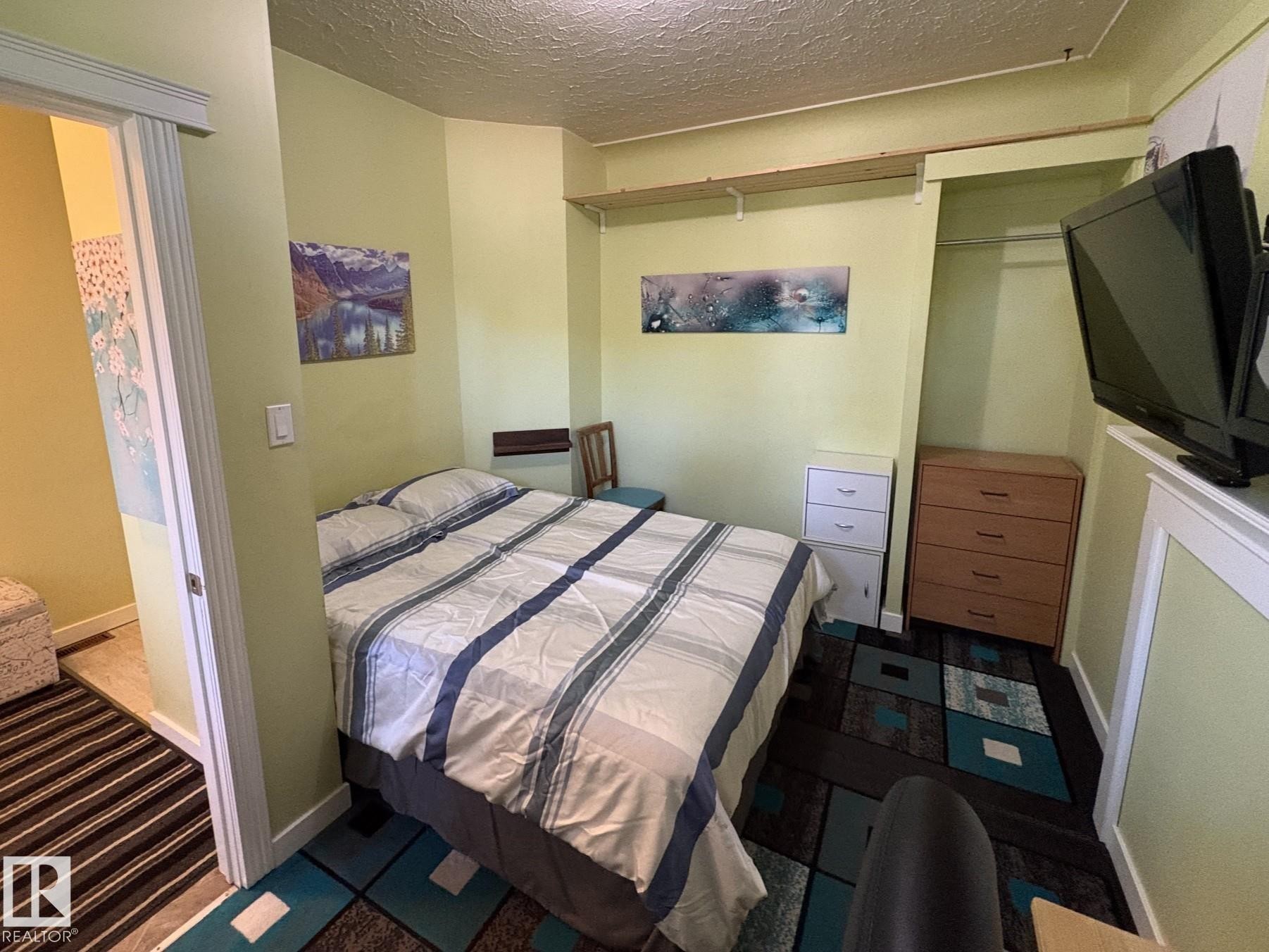 Compact room featuring light green walls, built-in shelving, and a patterned area rug - 11511 101 Street, Edmonton, AB