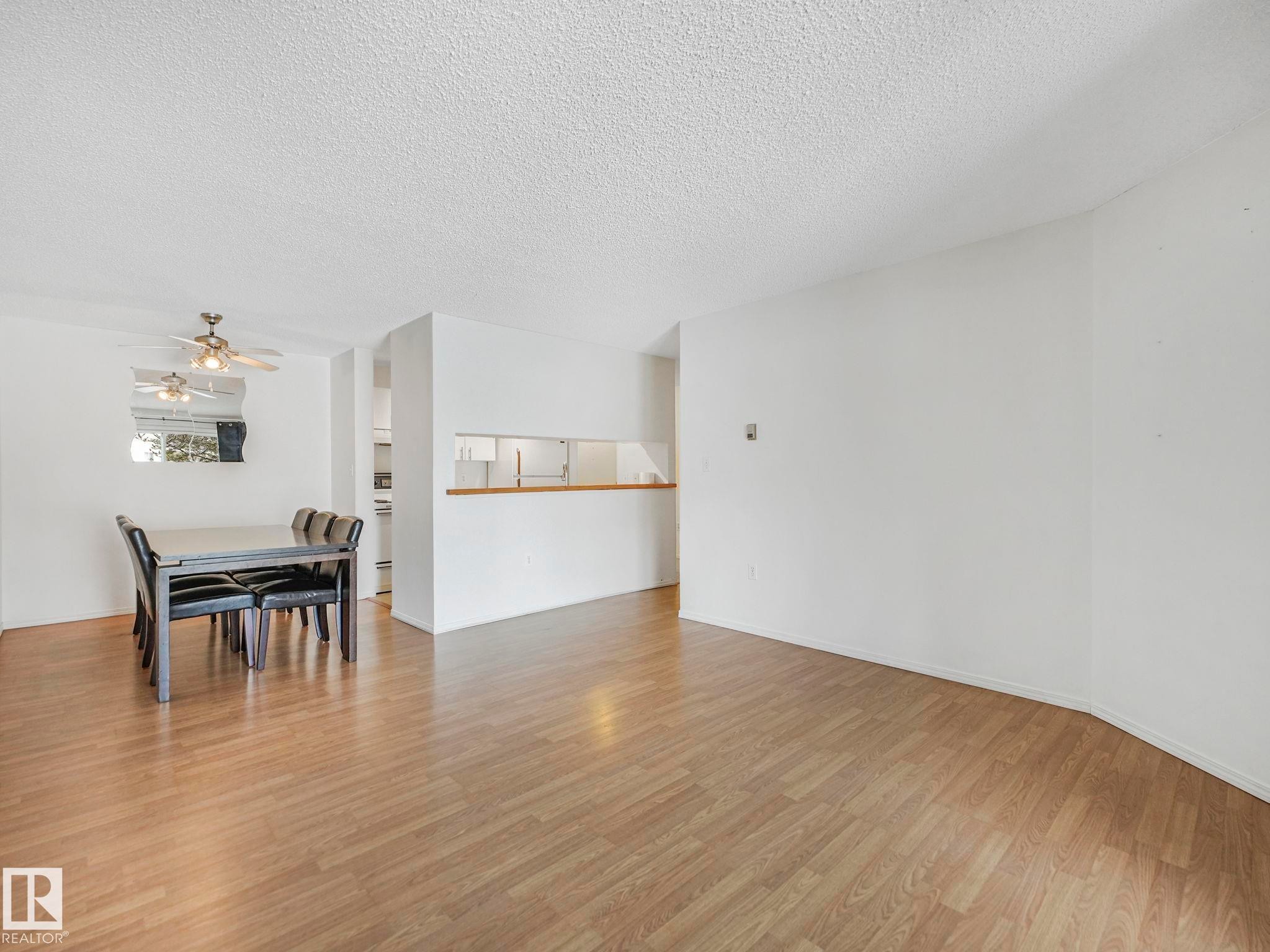 Spacious interior featuring wood-finish flooring, white walls, and a ceiling fan with integrated lighting - #143 10636 120 St Nw, Edmonton, AB - Indoor