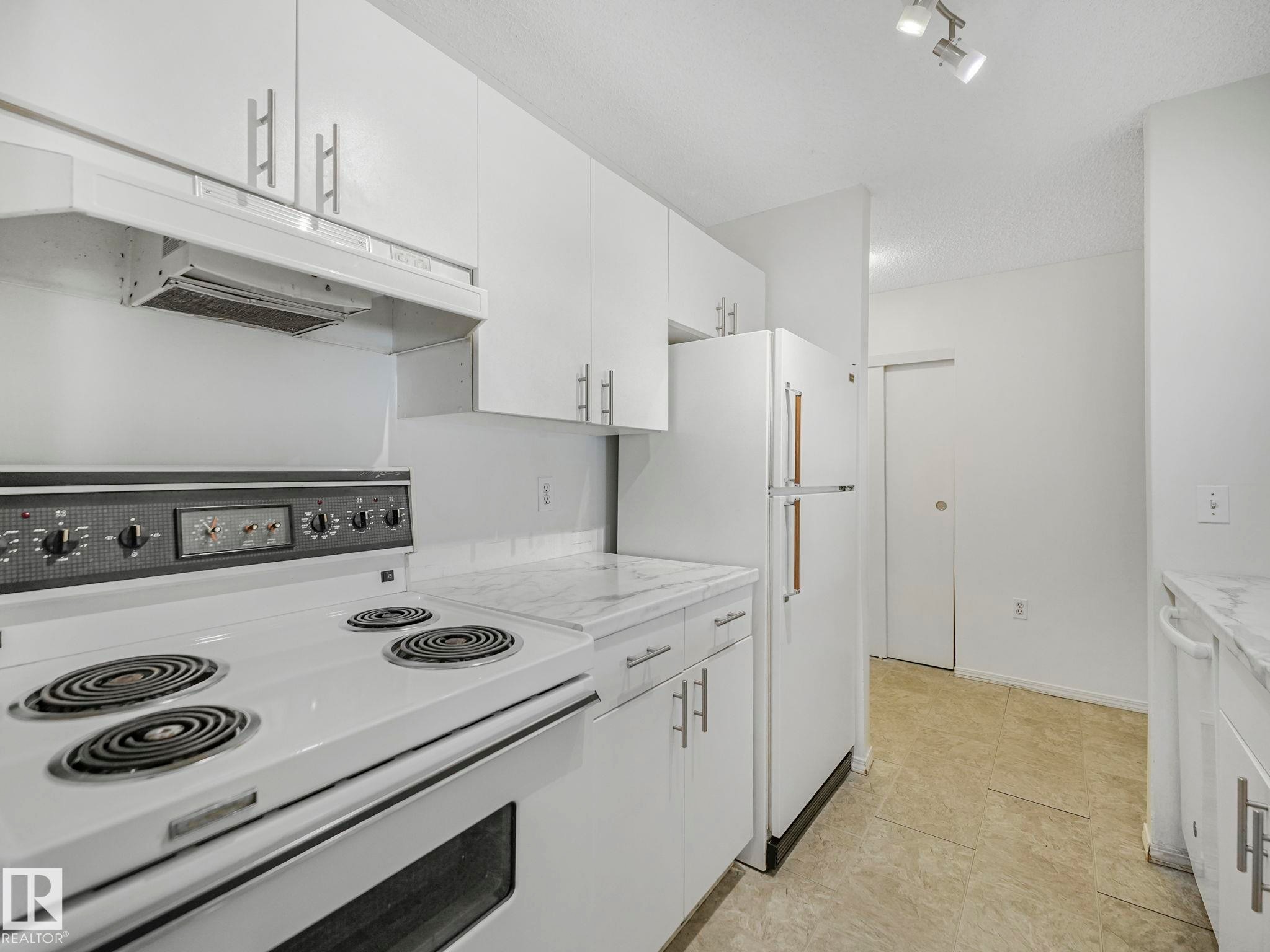 Kitchen featuring white cabinetry with silver-tone hardware, white range, white refrigerator, and light-toned countertop surfaces - #143 10636 120 St Nw, Edmonton, AB - Indoor Photo Showing Kitchen