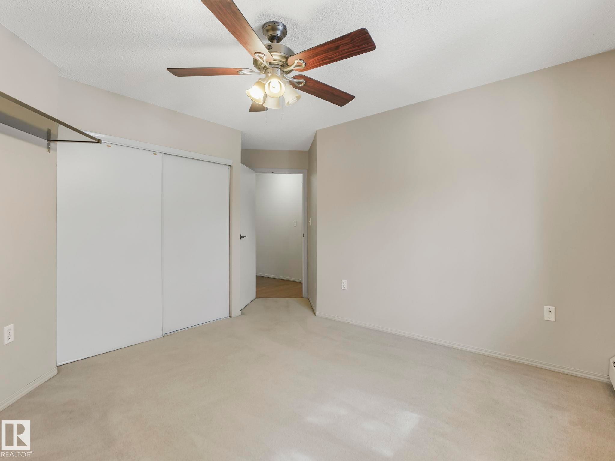 Bedroom featuring light neutral walls, carpeted flooring, a ceiling fan with integrated lighting, and sliding closet doors - #143 10636 120 St Nw, Edmonton, AB - Indoor Photo Showing Other Room
