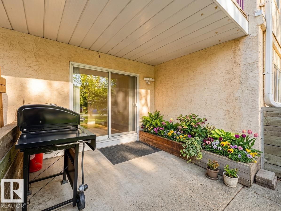 Private patio space featuring a concrete surface, a sliding glass door, and stucco exterior - #143 10636 120 St Nw, Edmonton, AB - Outdoor With Deck Patio Veranda With Exterior