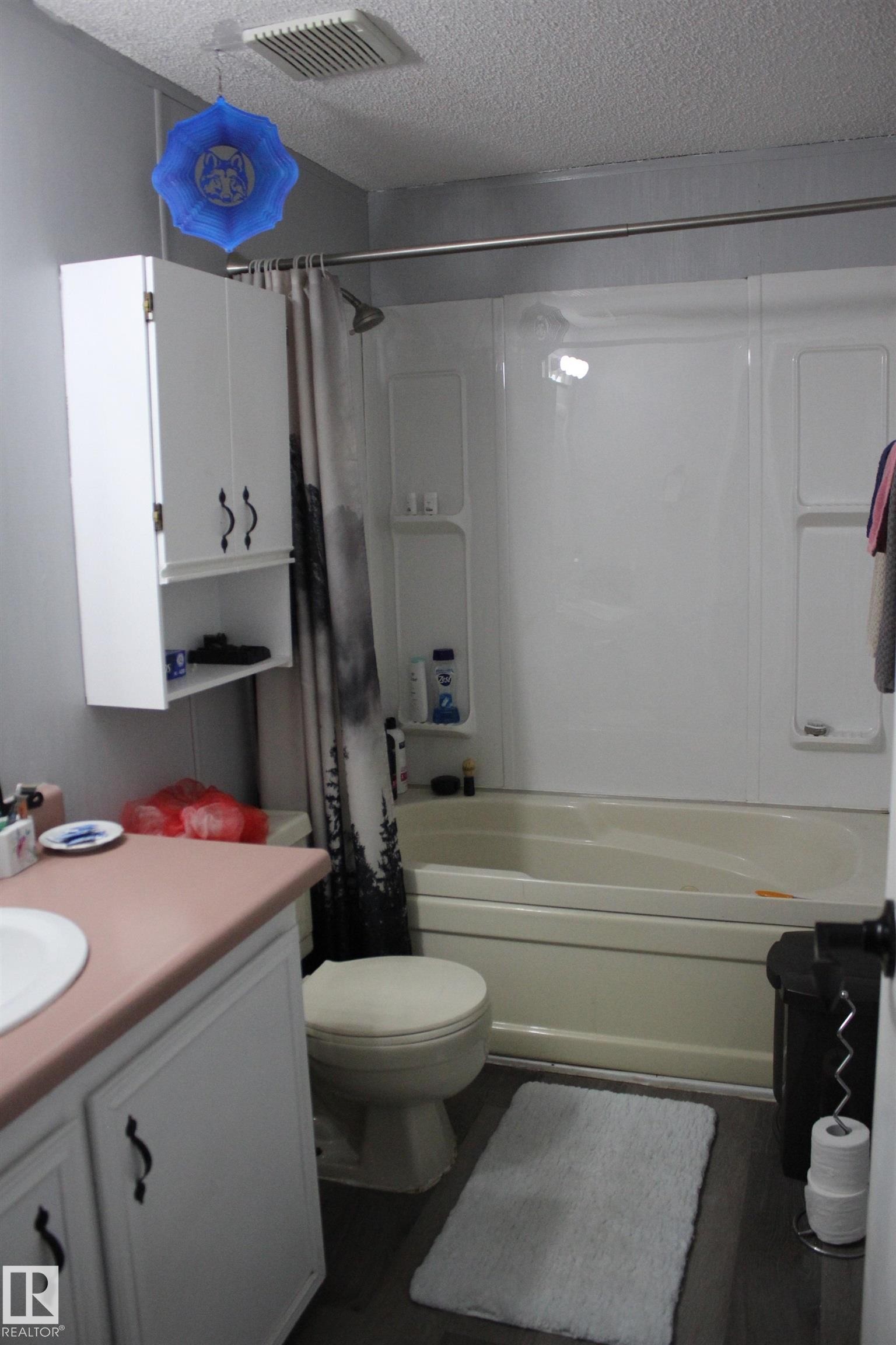 Full bathroom featuring a shower-tub combination with a white surround, white vanity cabinetry with dark hardware, a light pink countertop with an integrated sink, and wood-finish flooring - 4839 49 Avenue, Chipman, AB