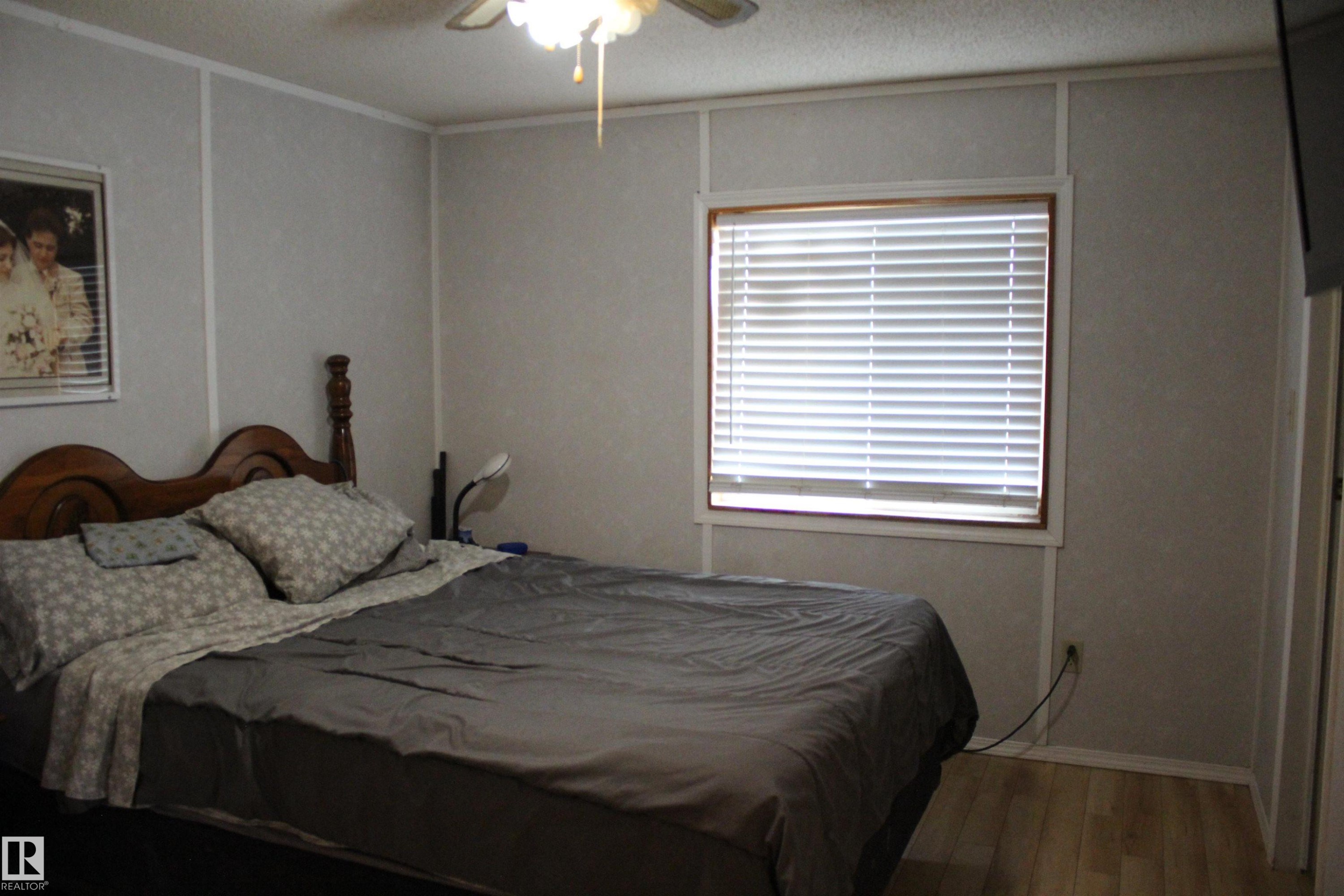 Bedroom featuring wood-finish flooring, a window with blinds, and a ceiling fan with integrated lighting - 4839 49 Avenue, Chipman, AB