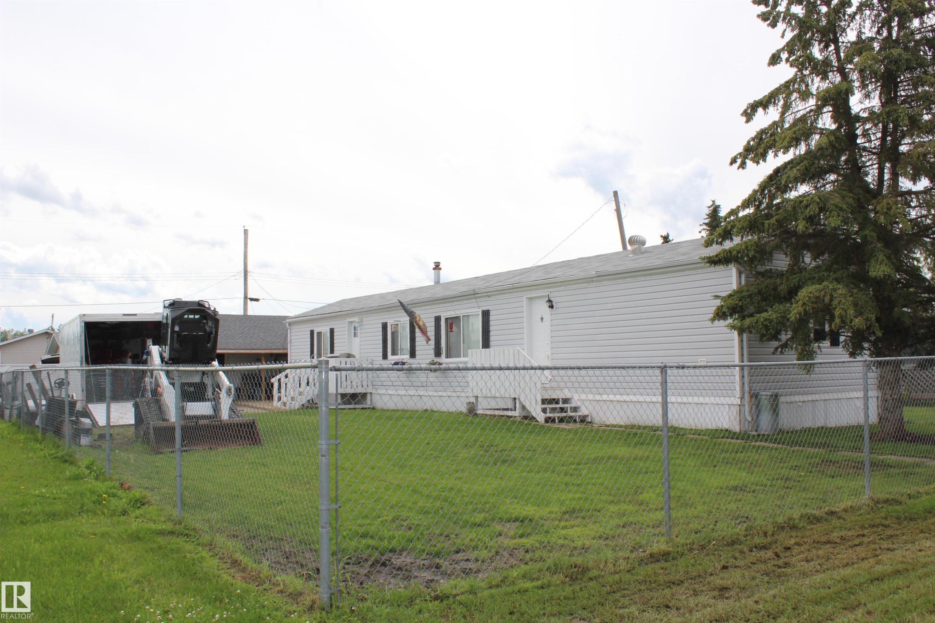 Exterior featuring white siding, a chain-link fence, and a mature evergreen tree - 4839 49 Avenue, Chipman, AB