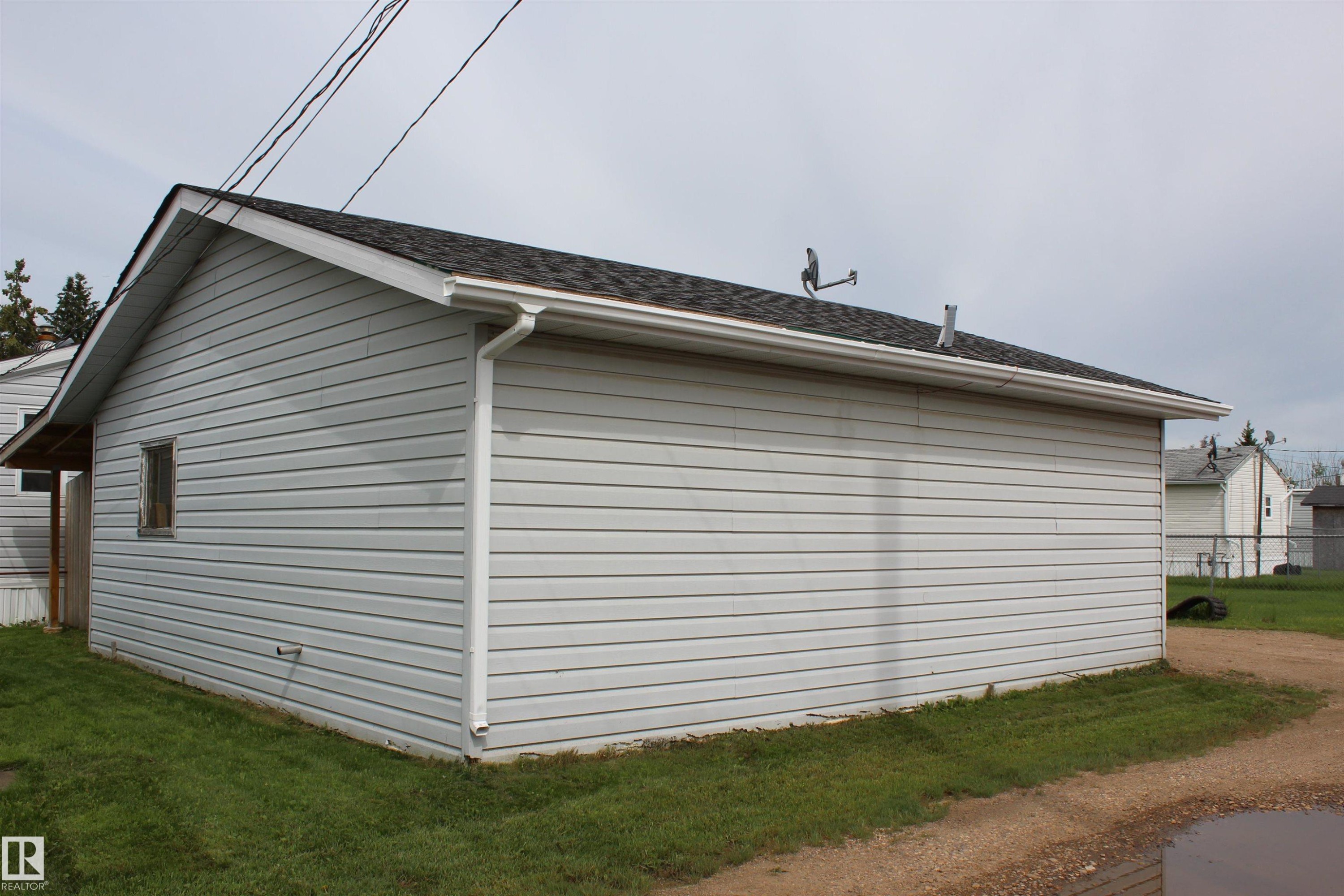 Detached garage featuring horizontal siding, a gabled roof with dark shingles, and white gutters - 4839 49 Avenue, Chipman, AB