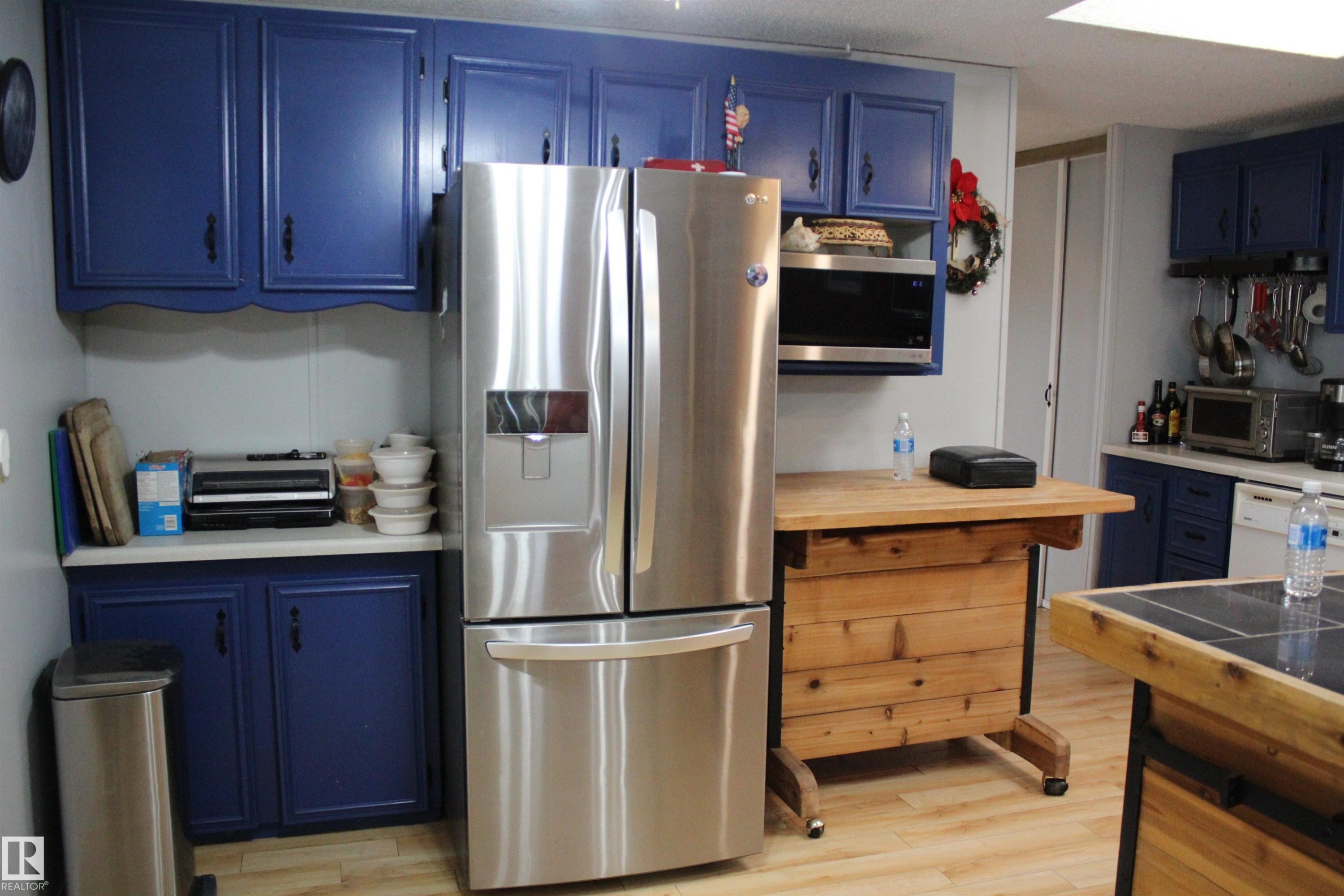 Kitchen featuring blue cabinetry, stainless steel refrigerator, built-in microwave, wood-finish flooring, and a mobile wood island - 4839 49 Avenue, Chipman, AB