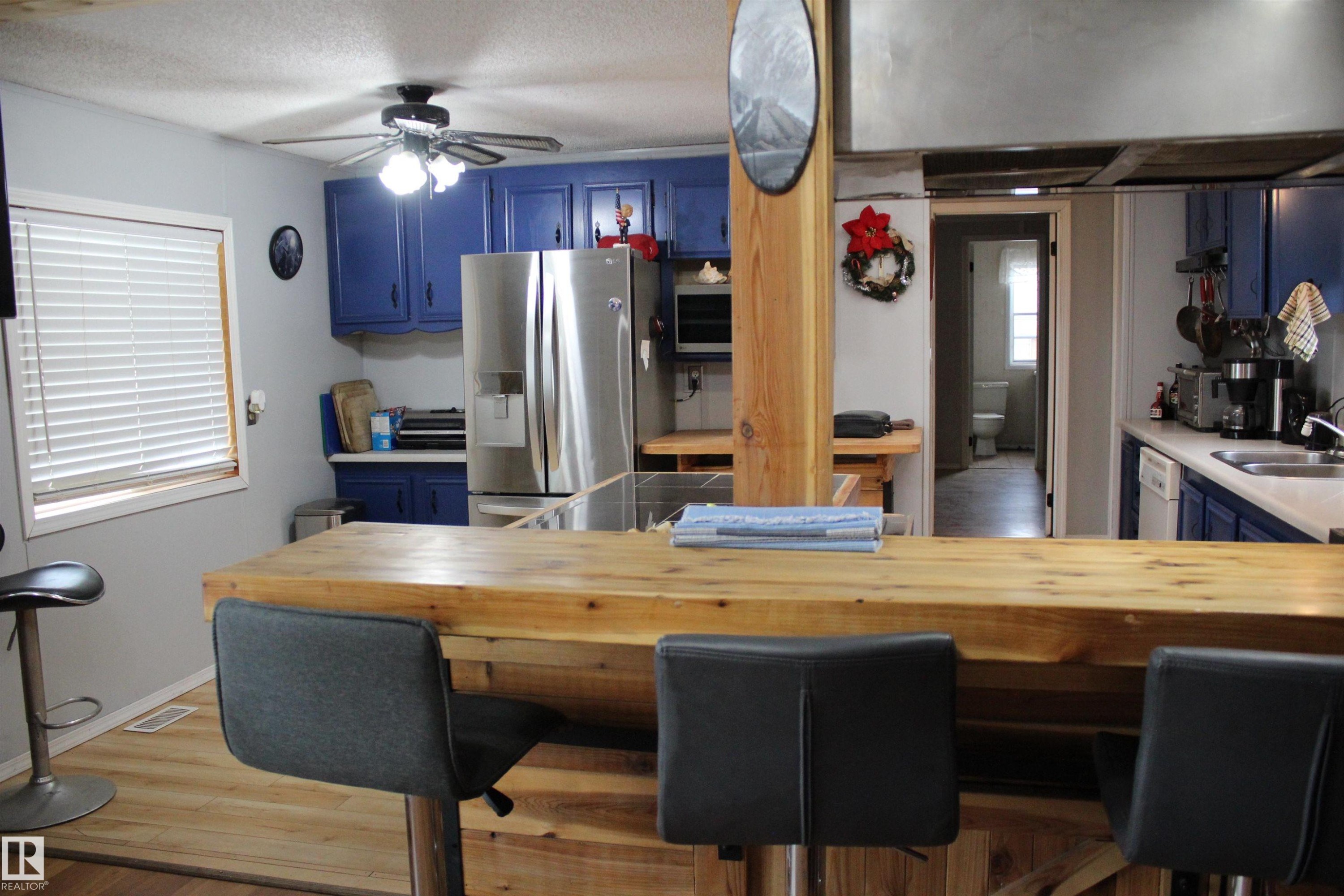 Kitchen featuring a wood-finish peninsula with seating, blue cabinetry, stainless steel refrigerator, and wood-finish flooring - 4839 49 Avenue, Chipman, AB