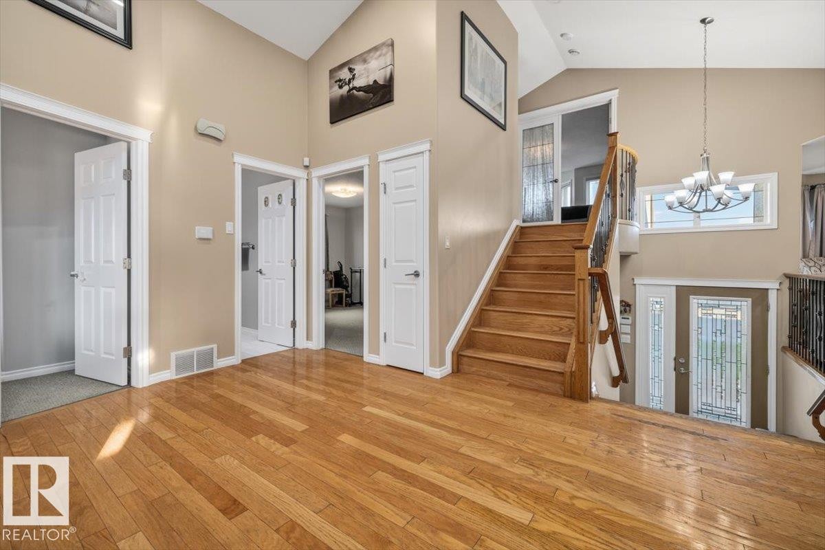 Entryway featuring wood-finish flooring, a grand staircase with wood railing and wrought iron spindles, high vaulted ceilings, and multiple doorways - 6050 164A Avenue, Edmonton, AB