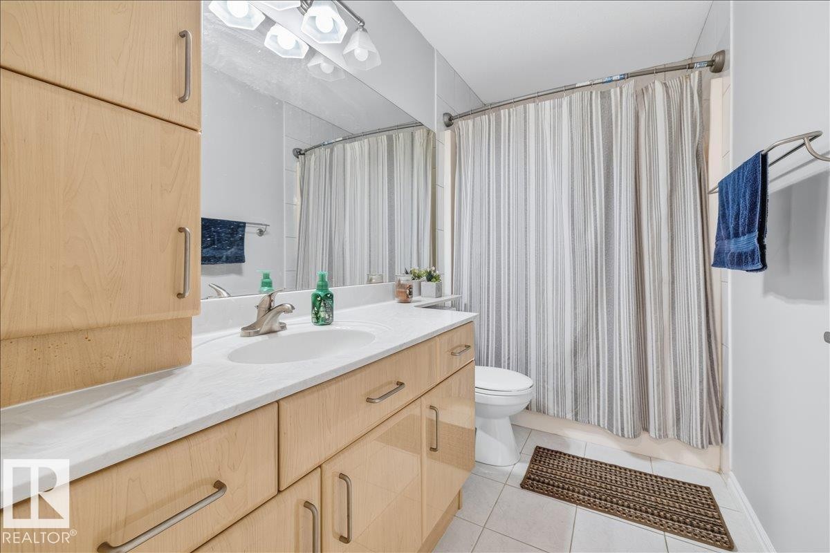 Bathroom featuring a light wood-finish vanity with a single basin sink, light-toned countertop, and ample storage cabinetry - 6050 164A Avenue, Edmonton, AB
