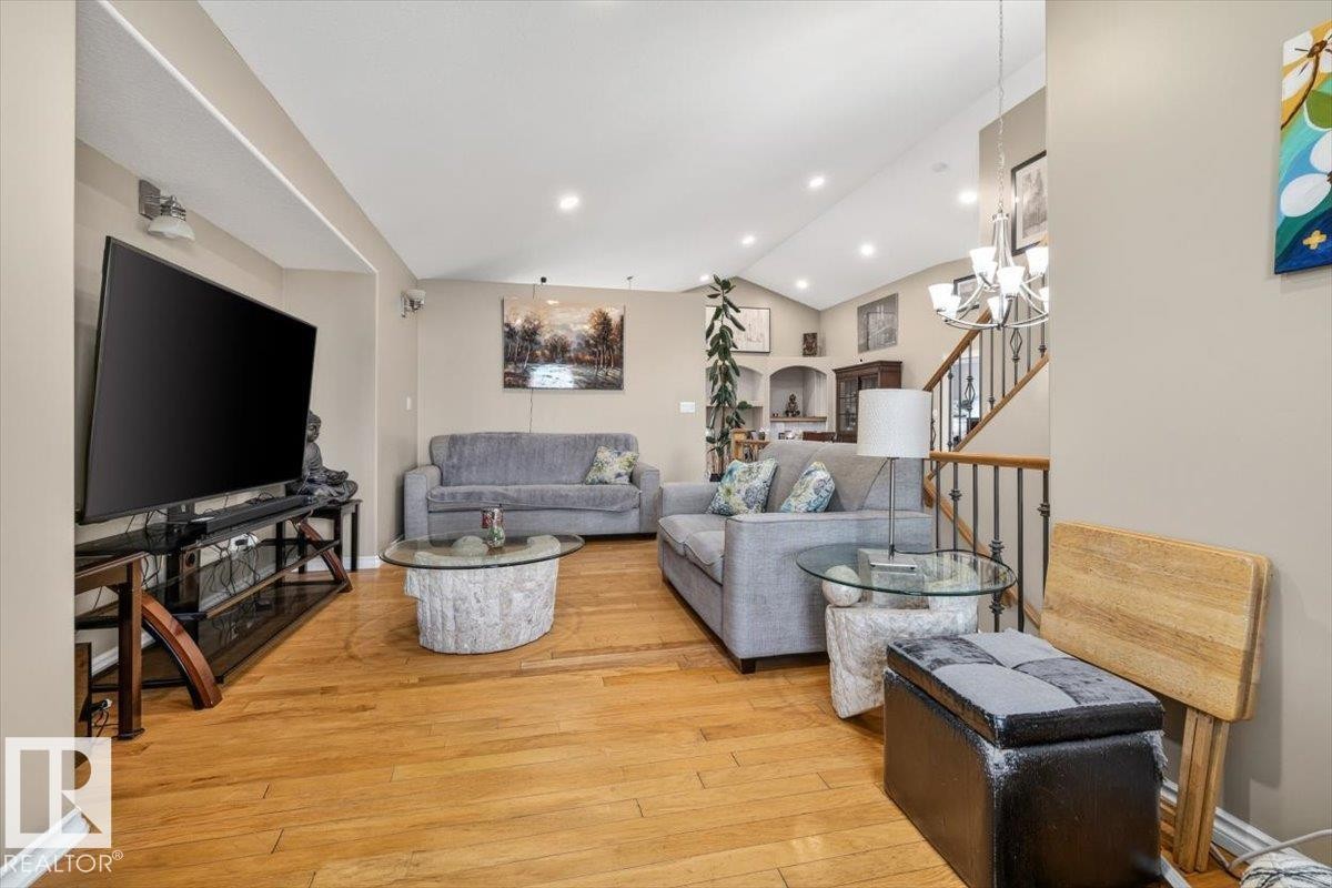 Open-concept living area featuring hardwood flooring, recessed ceiling lighting, a vaulted ceiling, and a staircase with wrought iron balusters - 6050 164A Avenue, Edmonton, AB