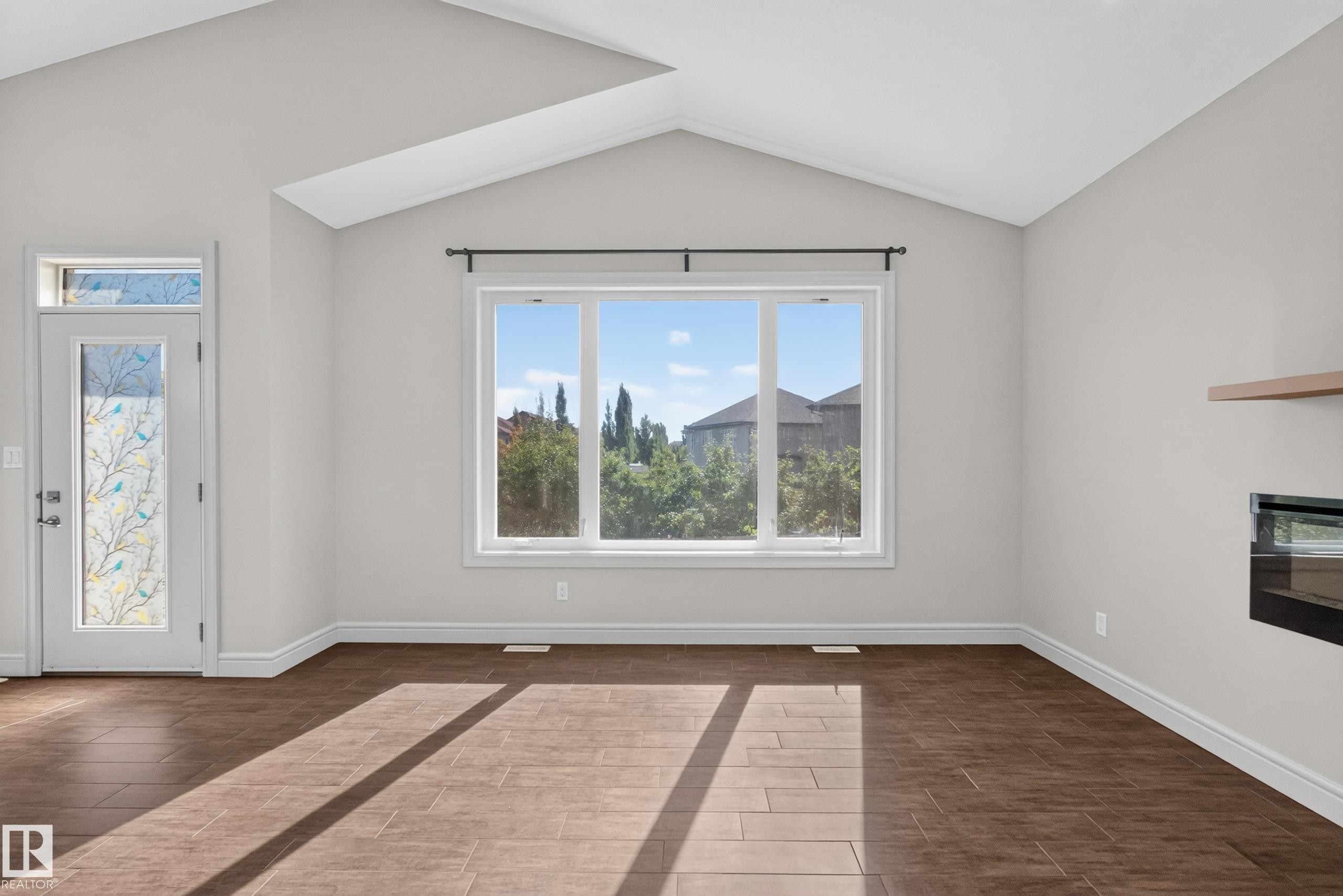 Spacious room featuring vaulted ceilings, a large multi-pane window, and wood-finish tile flooring - 1346 Cunningham Drive, Edmonton, AB
