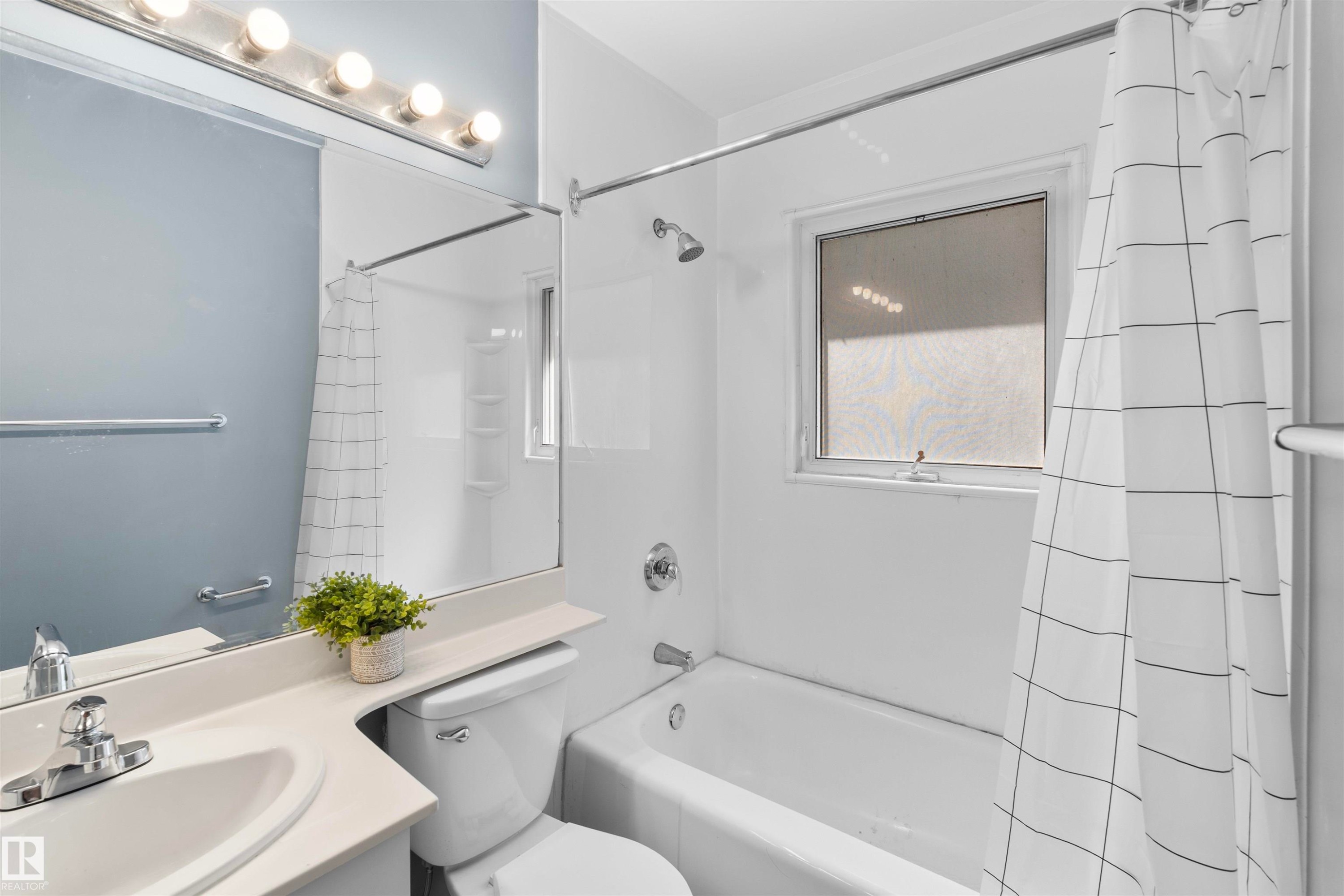 Bathroom featuring a white vanity with integrated sink, a large wall-mounted mirror, a five-light vanity fixture, and a tub/shower combination with a frosted window - 10607 73 Ave, Edmonton, AB