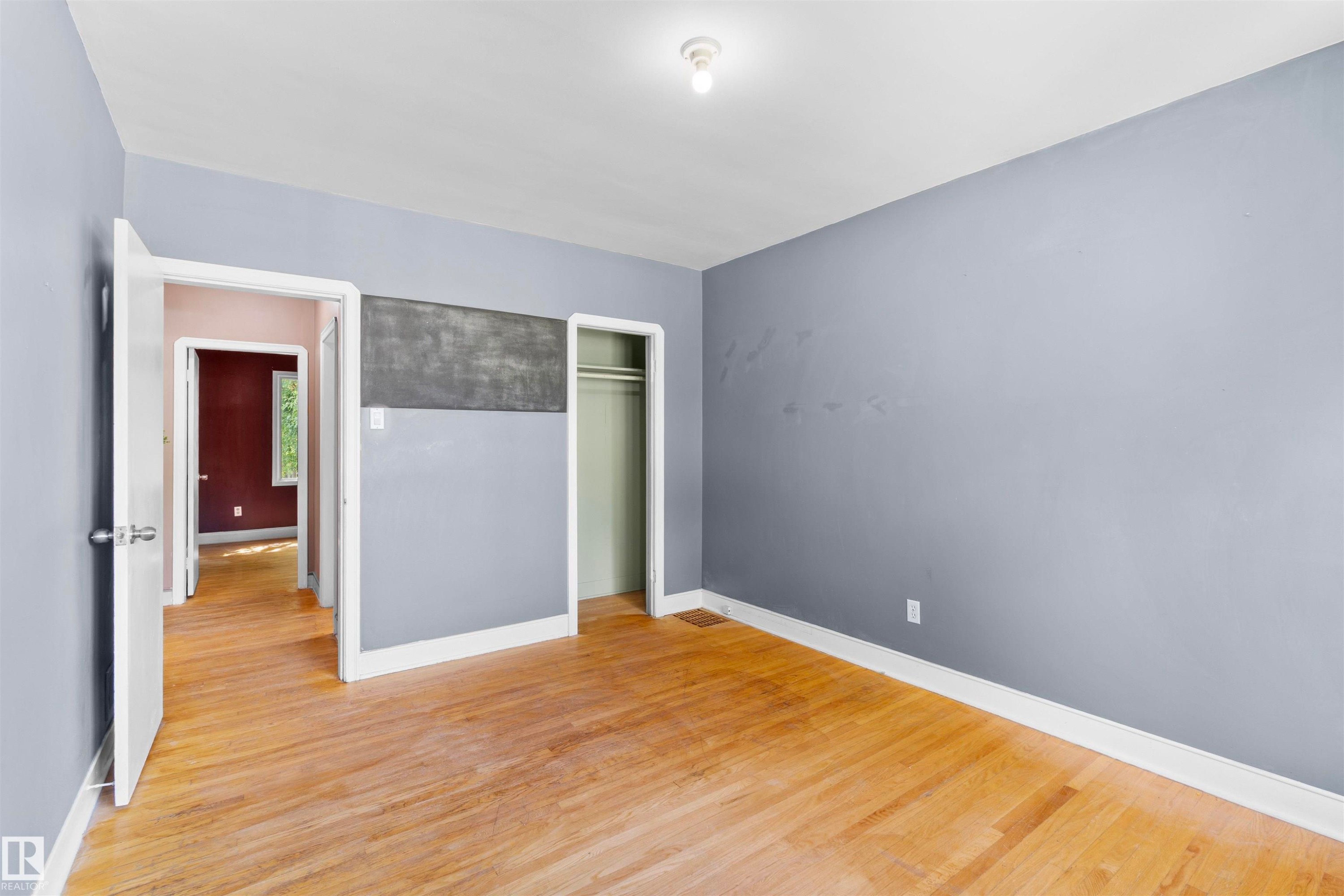 Hardwood flooring extends throughout this room, featuring light gray walls, white trim, and a recessed clothing rod - 10607 73 Ave, Edmonton, AB