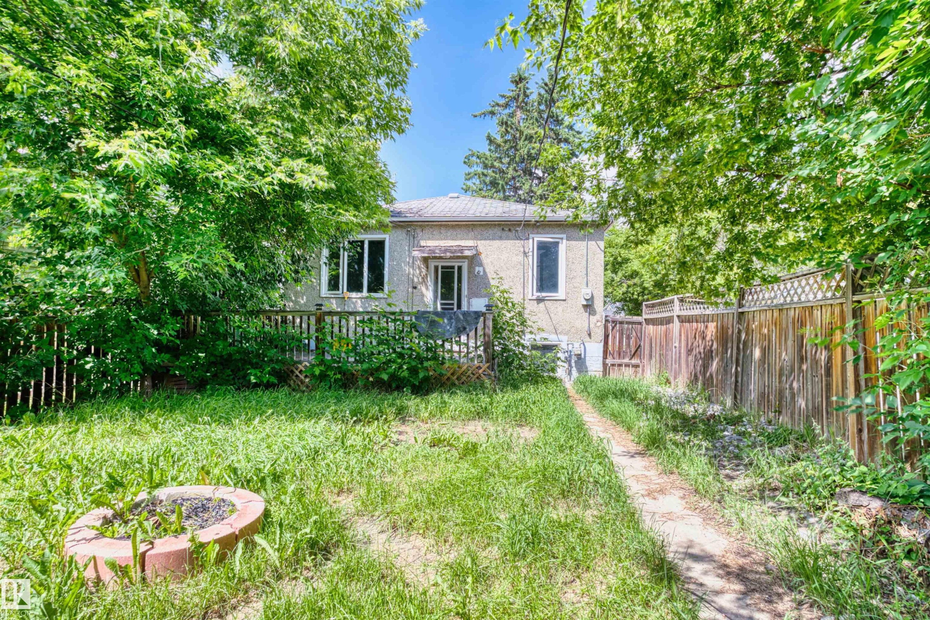 Rear exterior featuring a light-colored facade, multiple windows, and a covered entry - 10607 73 Ave, Edmonton, AB
