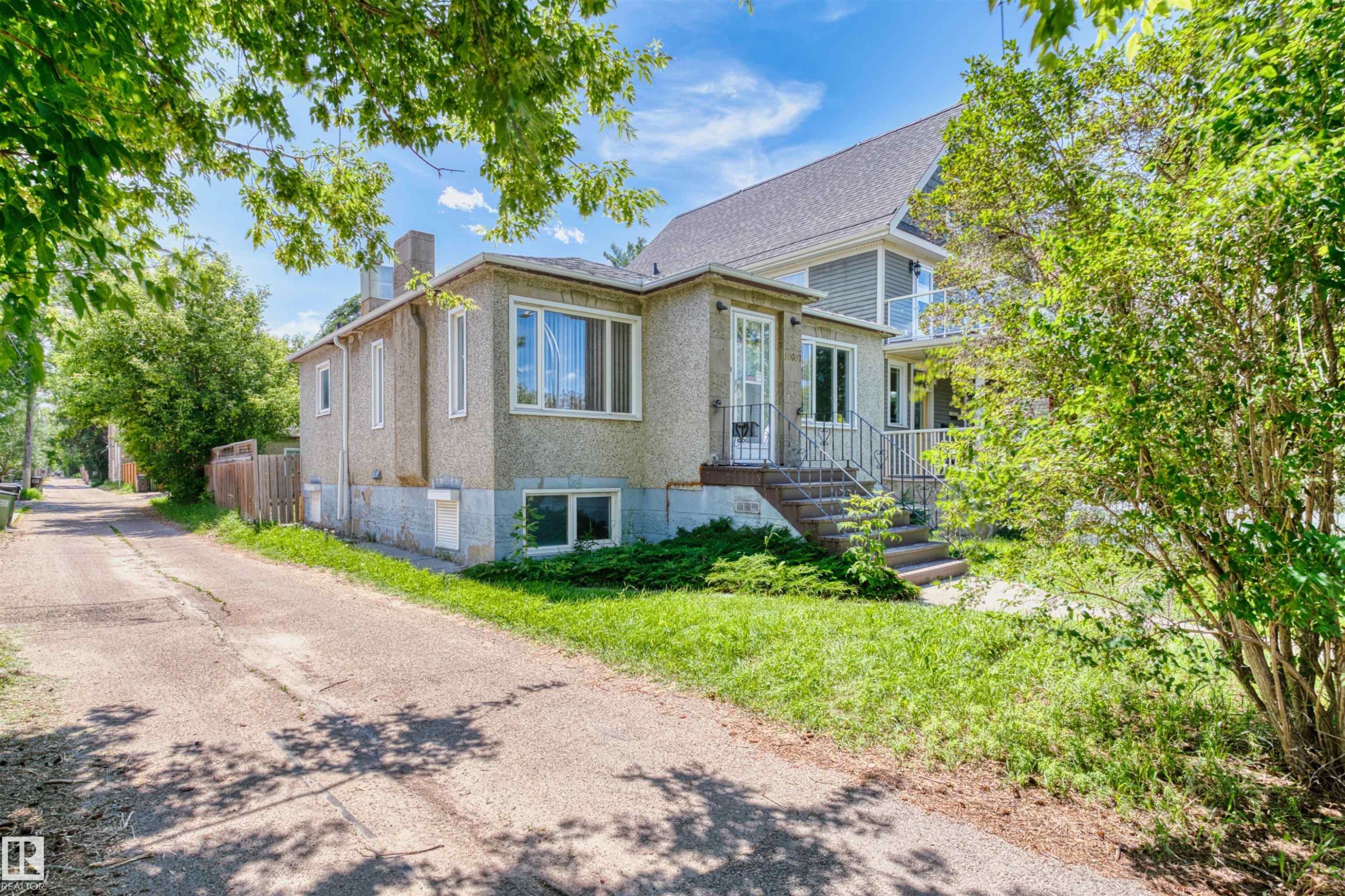 Split-level residence featuring a stucco exterior, a prominent front entrance with metal railings, and a secondary balcony with a glass railing - 10607 73 Ave, Edmonton, AB