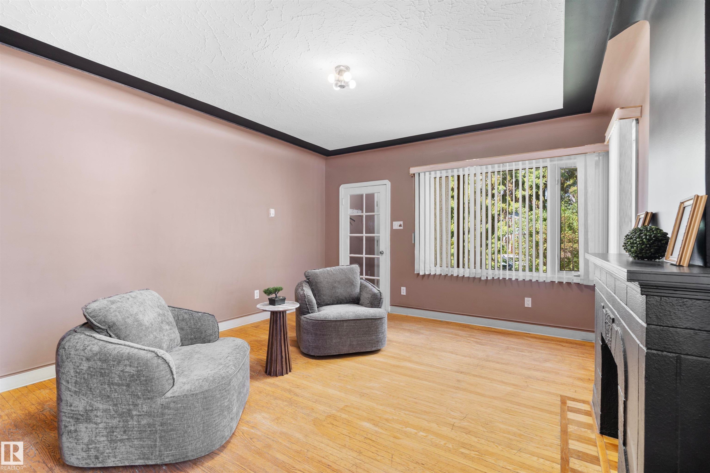 Living area featuring light wood-finish flooring and a corner fireplace with a dark-painted brick surround - 10607 73 Ave, Edmonton, AB