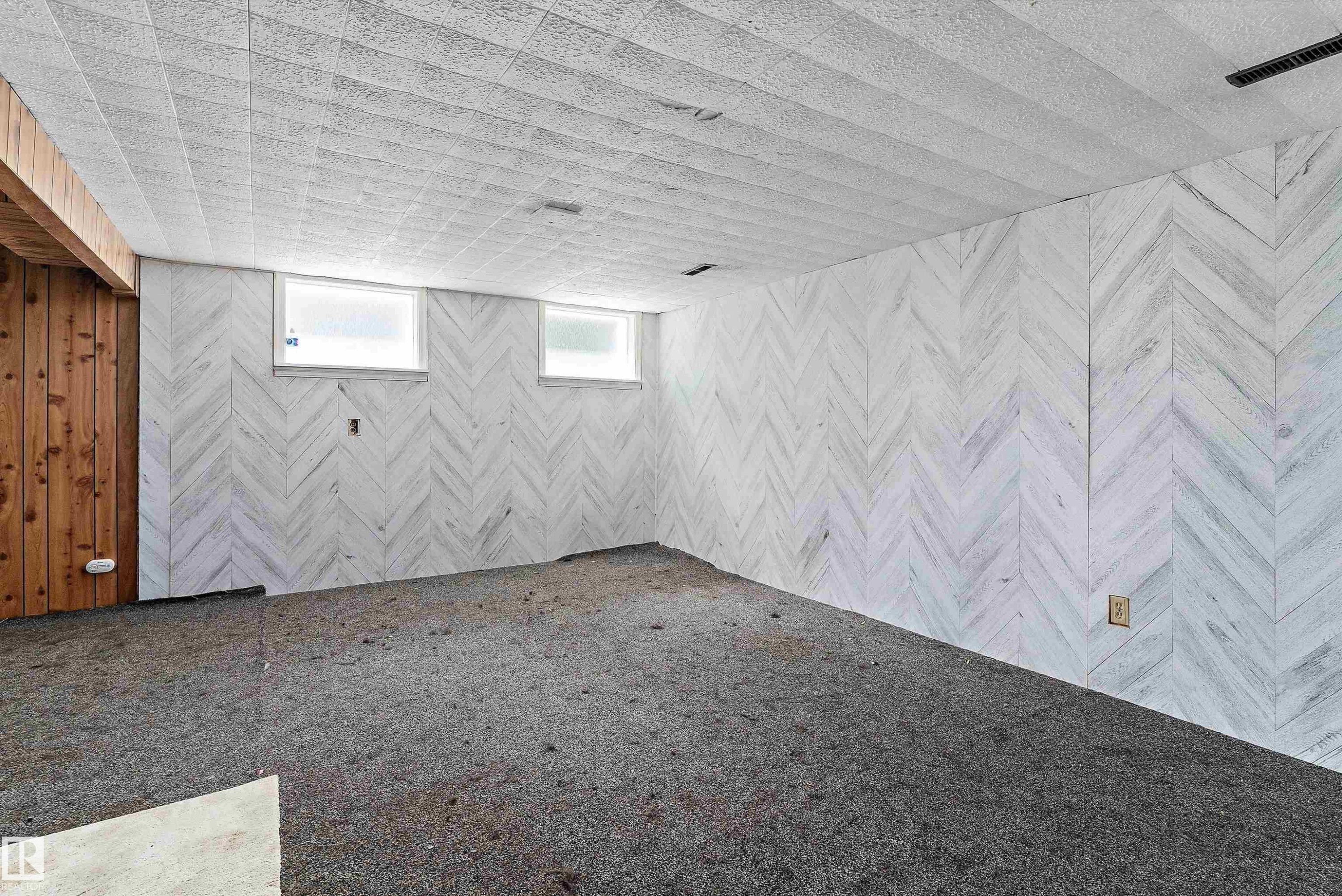 Finished room featuring chevron pattern wall paneling, a textured ceiling, and two small windows - 11619 123 Street, Edmonton, AB
