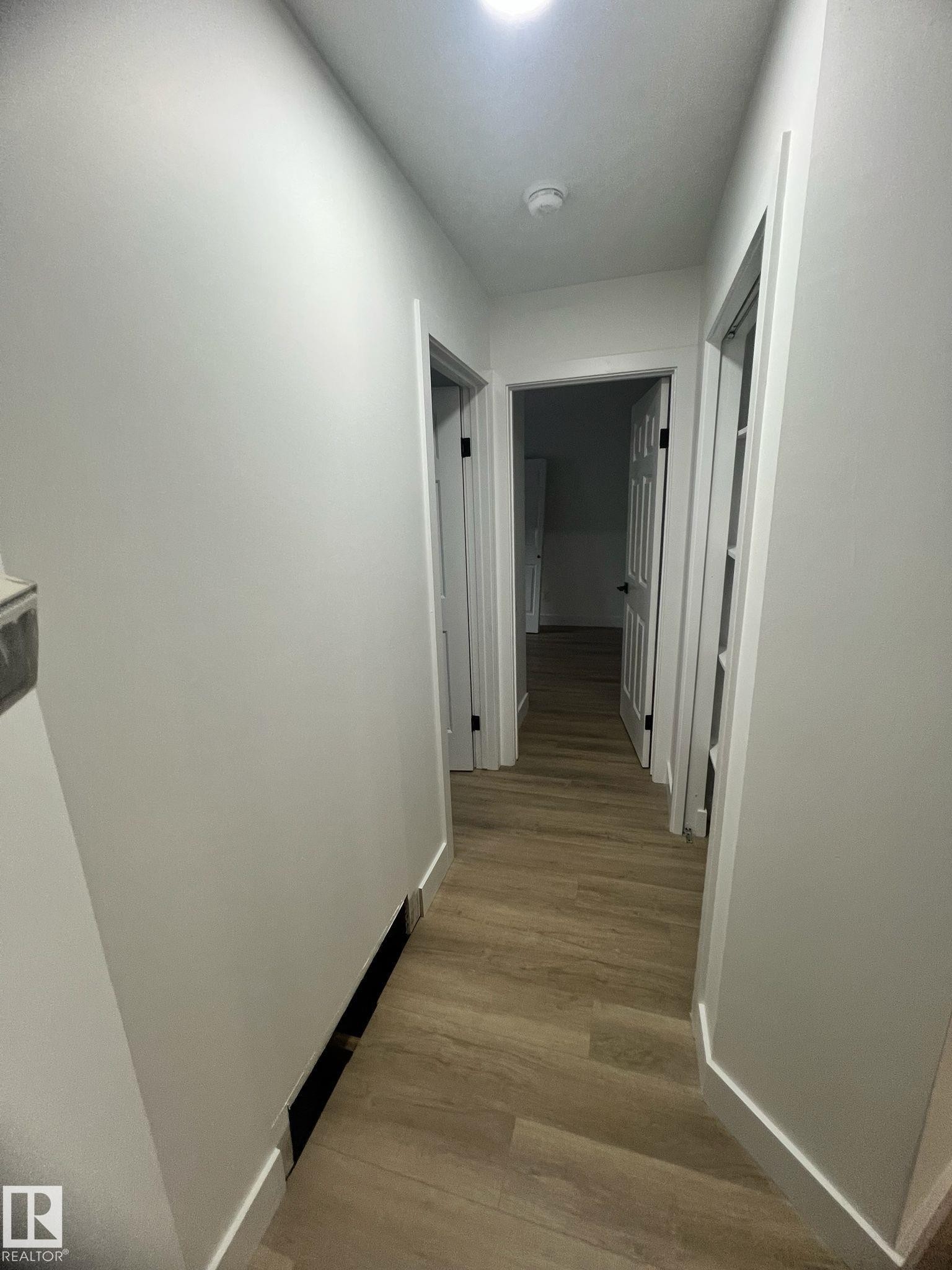 Hallway featuring wood-finish flooring, white painted walls, and multiple doorways with contrasting dark door hardware - 3320 43 Street, Edmonton, AB