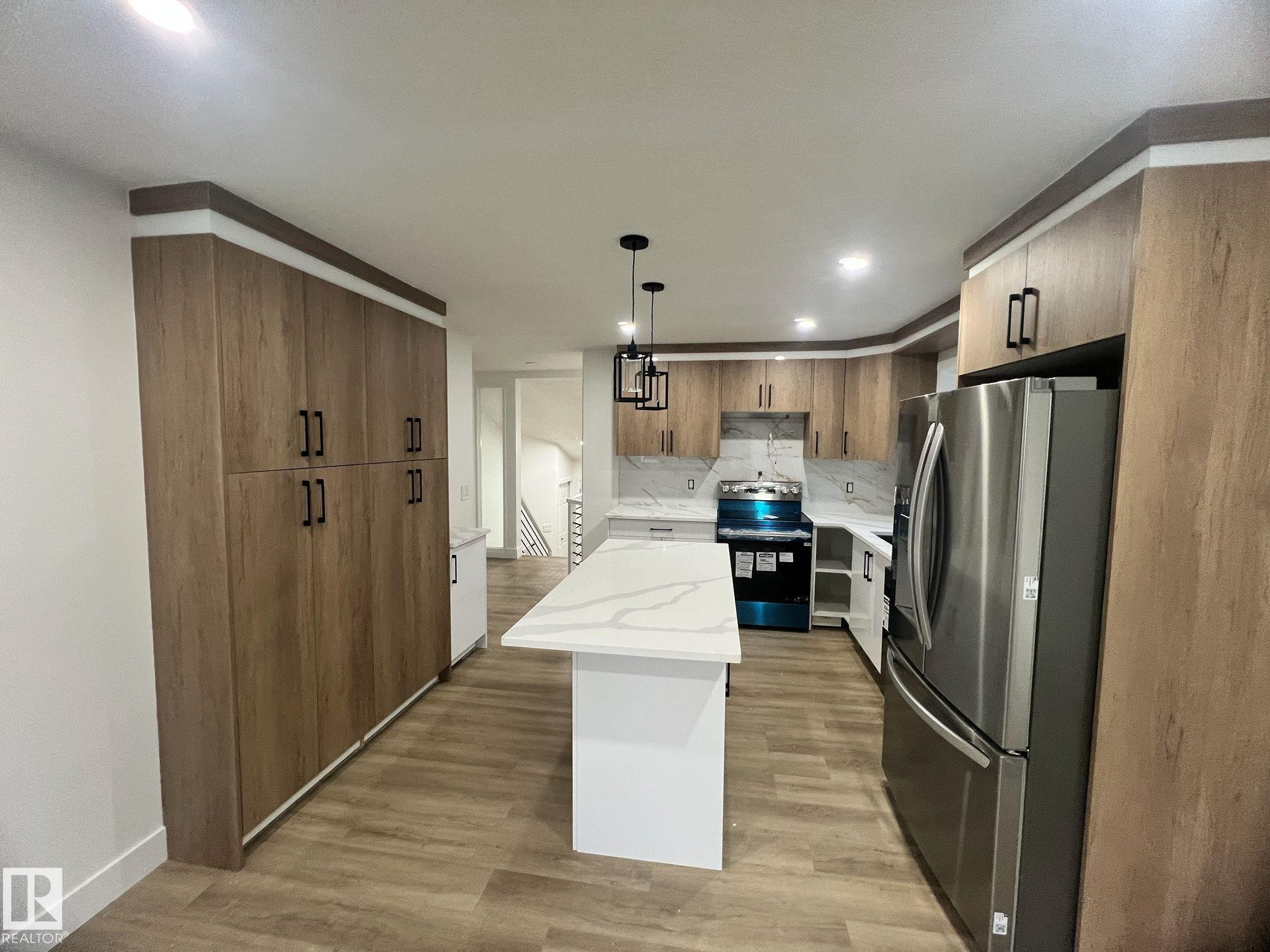 Kitchen featuring wood-finish cabinetry, stainless steel refrigerator, white quartz countertops, and coordinating backsplash - 3320 43 Street, Edmonton, AB