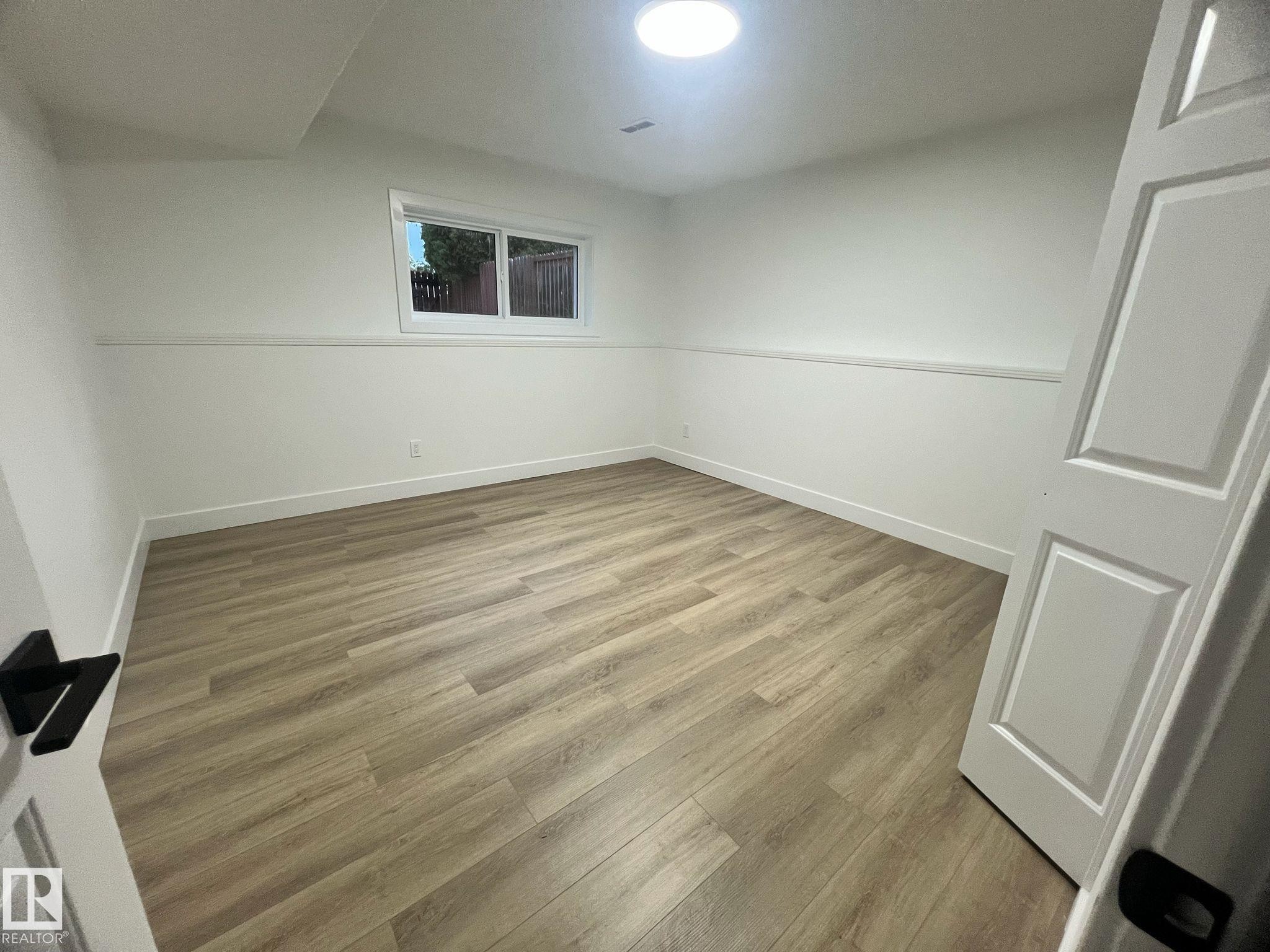 Spacious room featuring light wood-finish flooring, white walls with an accent trim, a window, and a ceiling-mounted light fixture - 3320 43 Street, Edmonton, AB