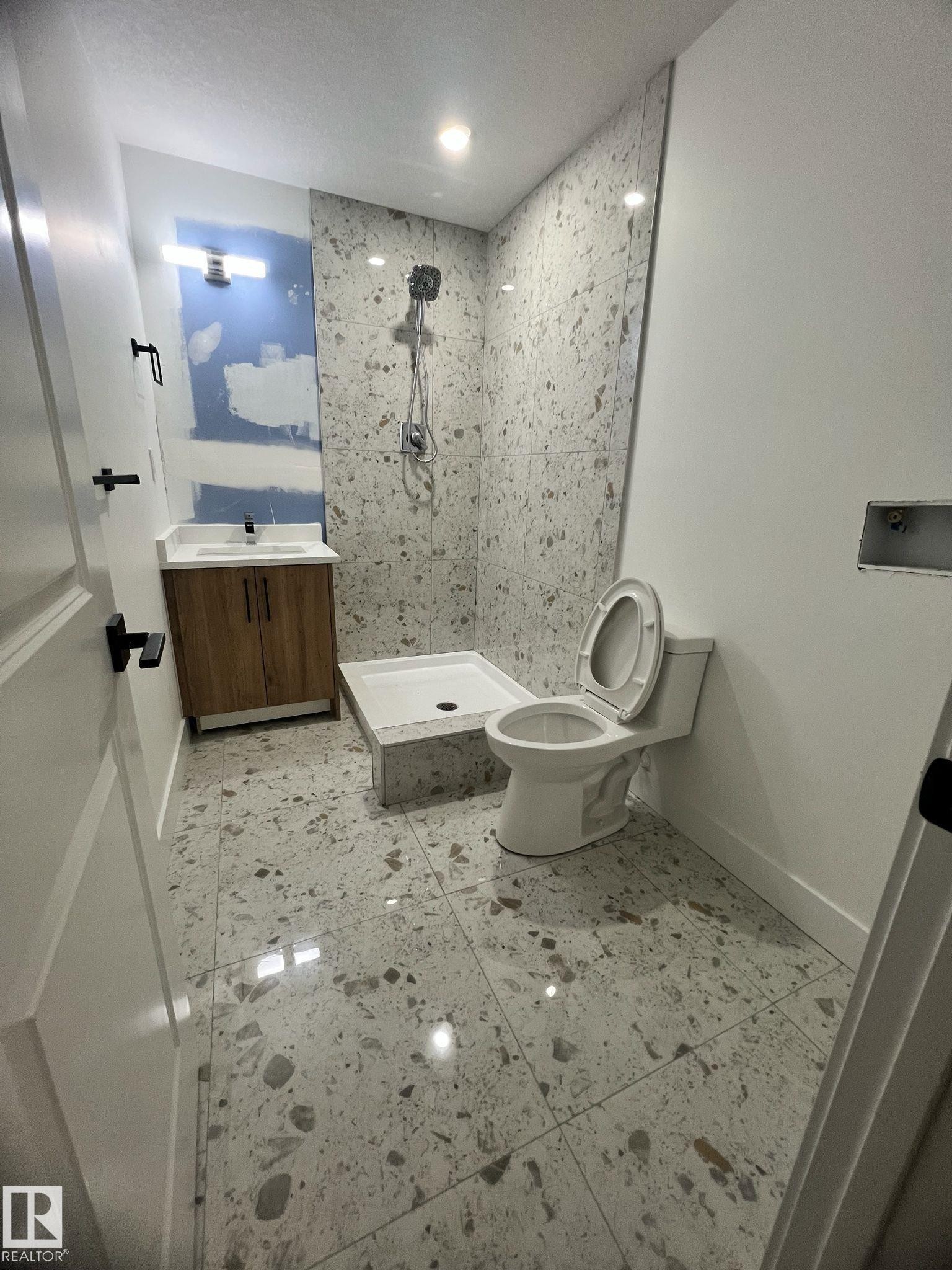 Contemporary bathroom featuring large format terrazzo-style floor tiles, a wood-finish vanity with an undermount sink, a white shower pan, and a tiled shower surround - 3320 43 Street, Edmonton, AB