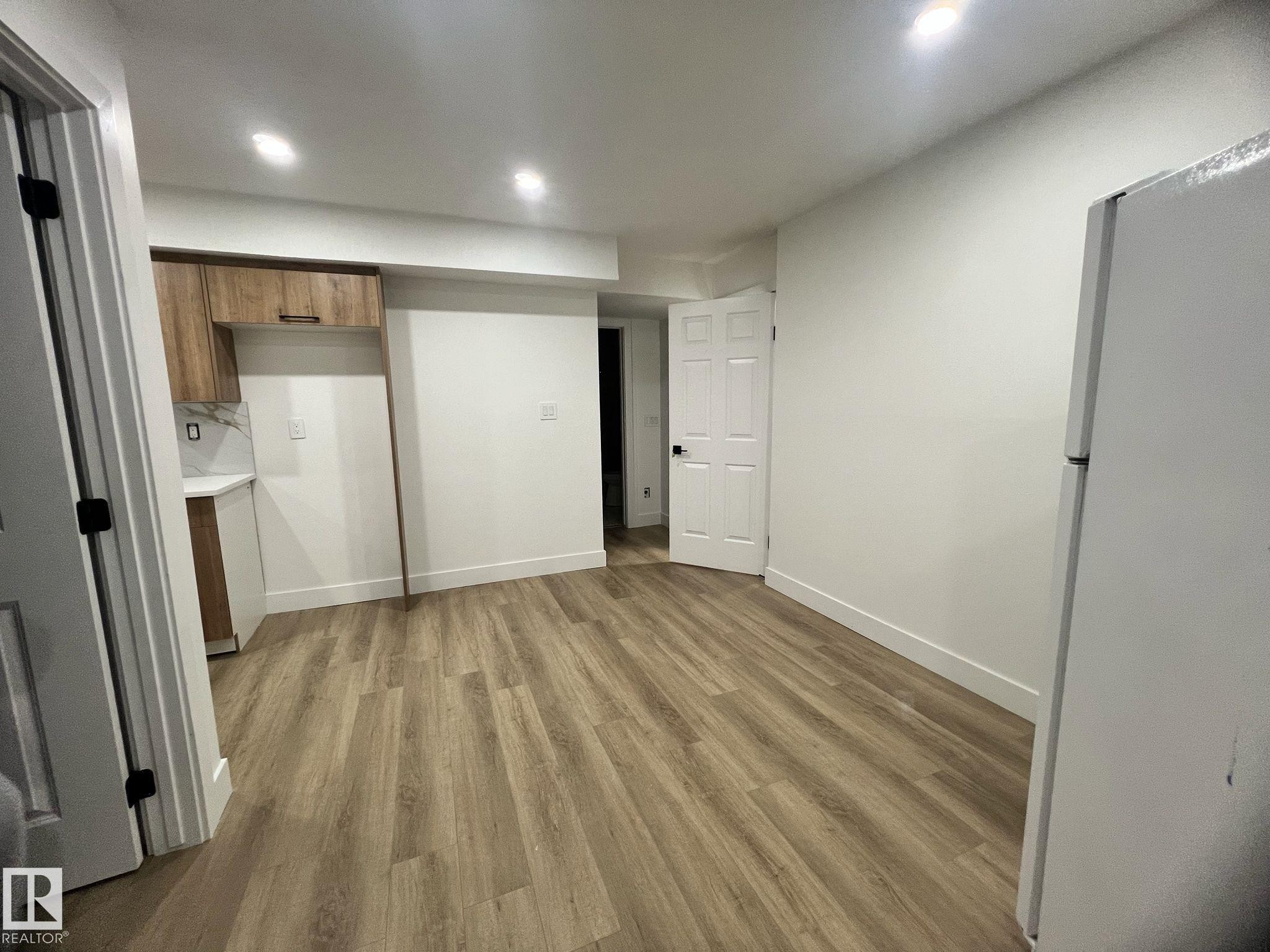 Wood-finish flooring throughout, featuring a kitchen corner with wood cabinetry, a light countertop, and a white tile backsplash - 3320 43 Street, Edmonton, AB