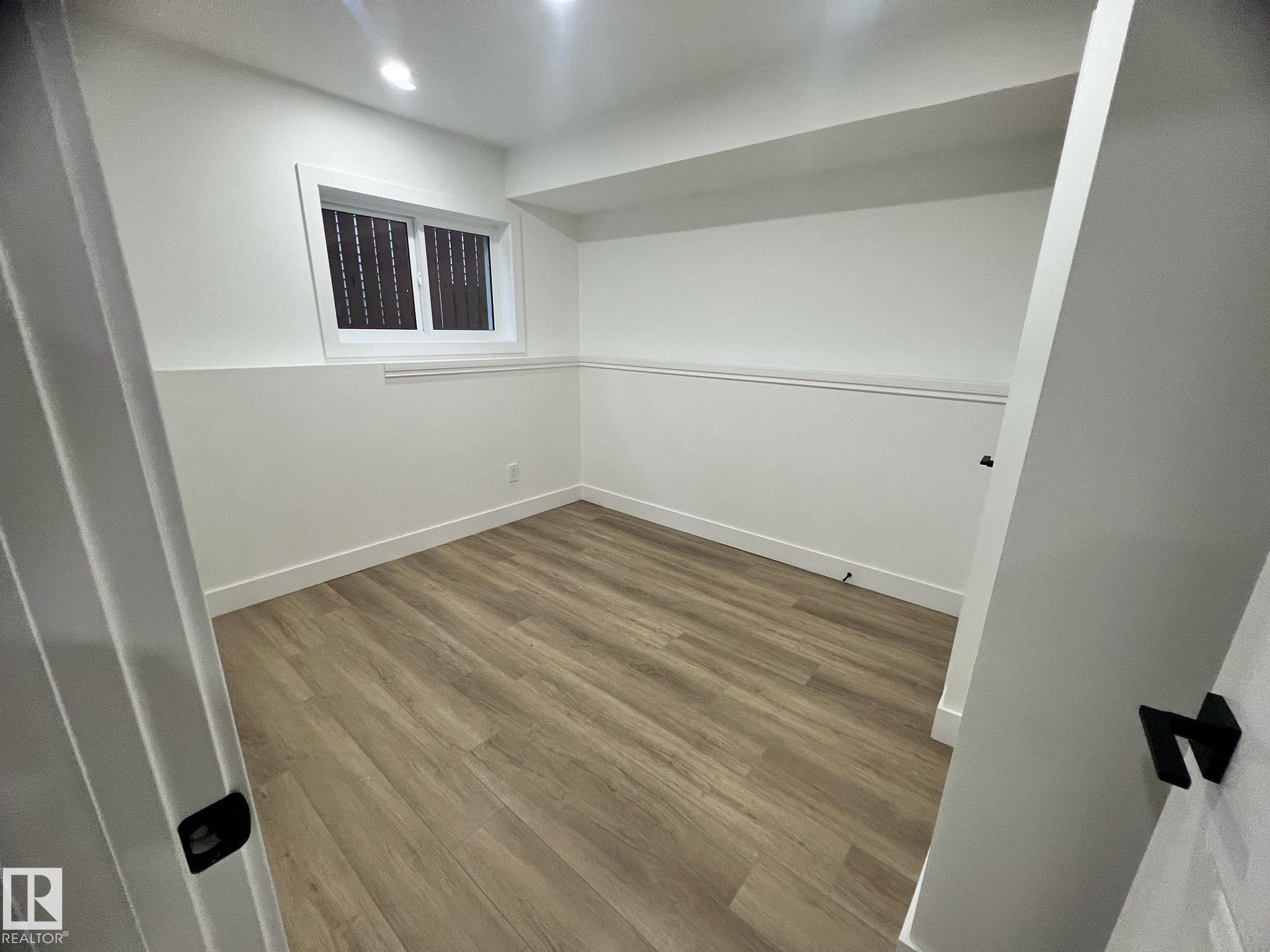 Room featuring wood-finish flooring, white painted walls, a window with horizontal blinds, and a white baseboard trim - 3320 43 Street, Edmonton, AB