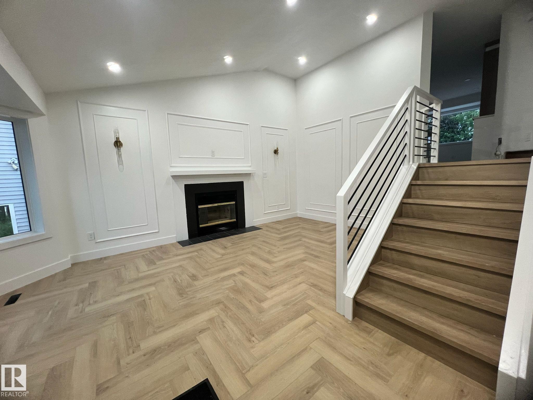 Living area featuring herringbone wood-finish flooring, a fireplace with a black surround and hearth, and decorative wall paneling - 3320 43 Street, Edmonton, AB