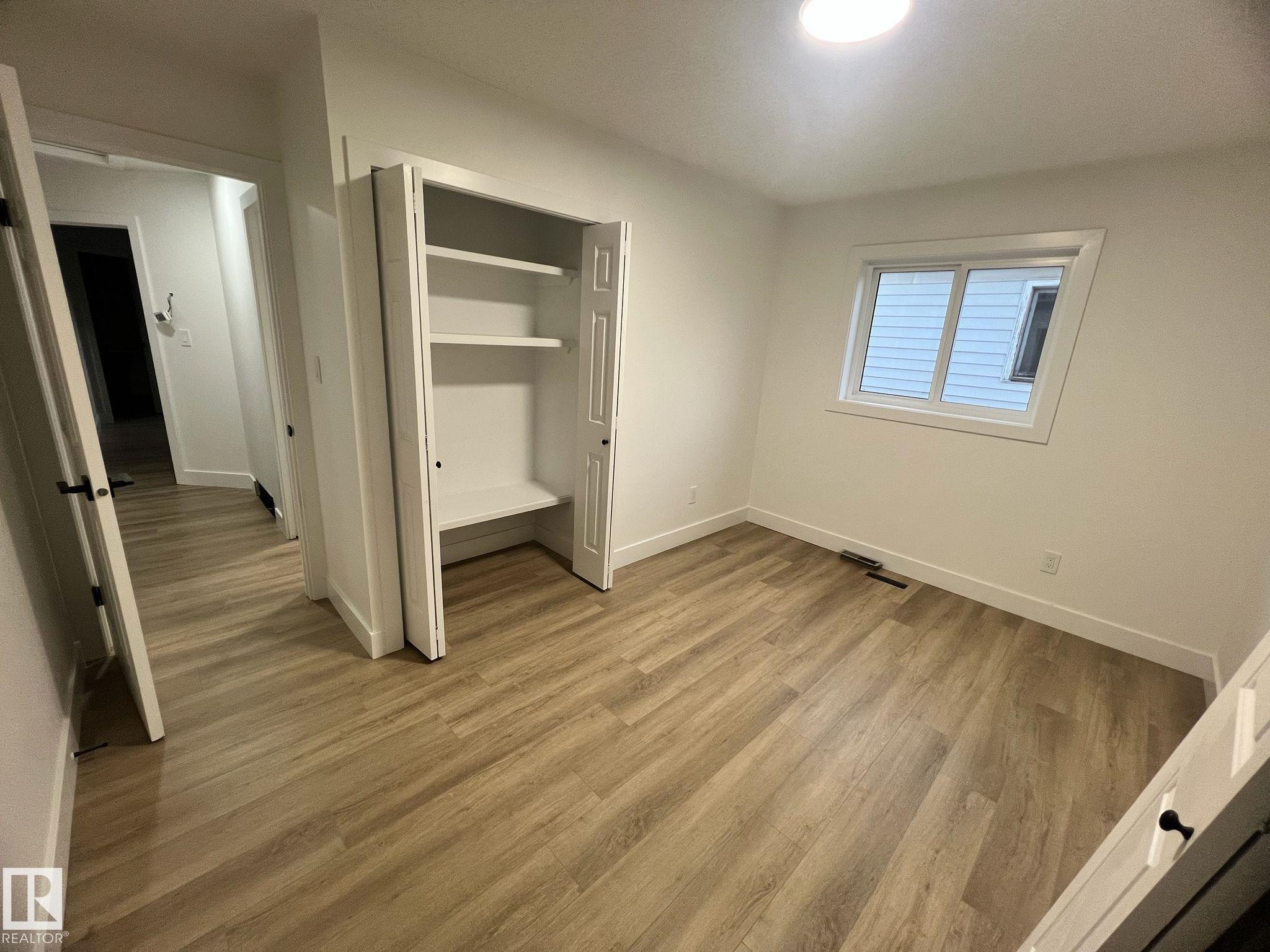 Neutral room with wood-finish flooring, a built-in closet with shelving, white trim, and a window providing natural illumination - 3320 43 Street, Edmonton, AB