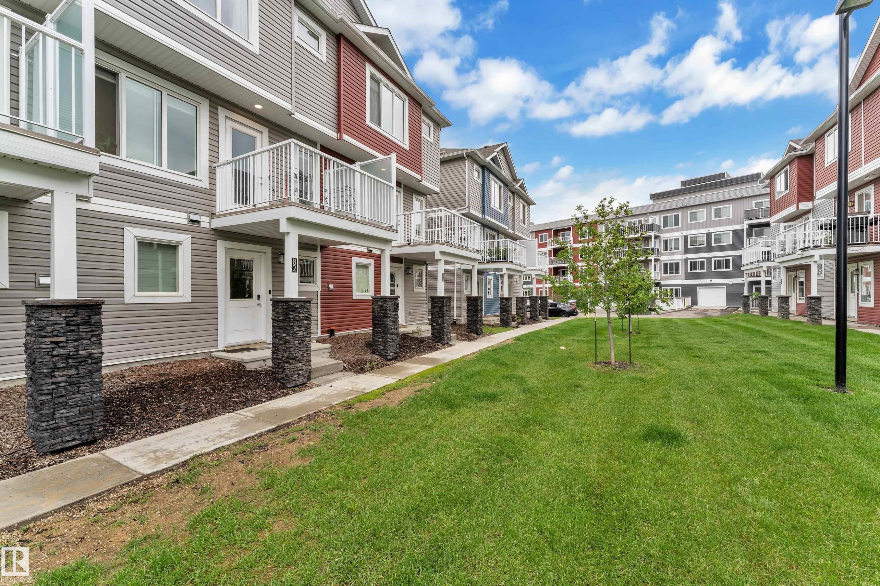 Modern townhome exteriors featuring horizontal siding in varied colors, stone pillar accents, and private balconies with white railings - #82 1816 Rutherford Rd Sw, Edmonton, AB - Outdoor