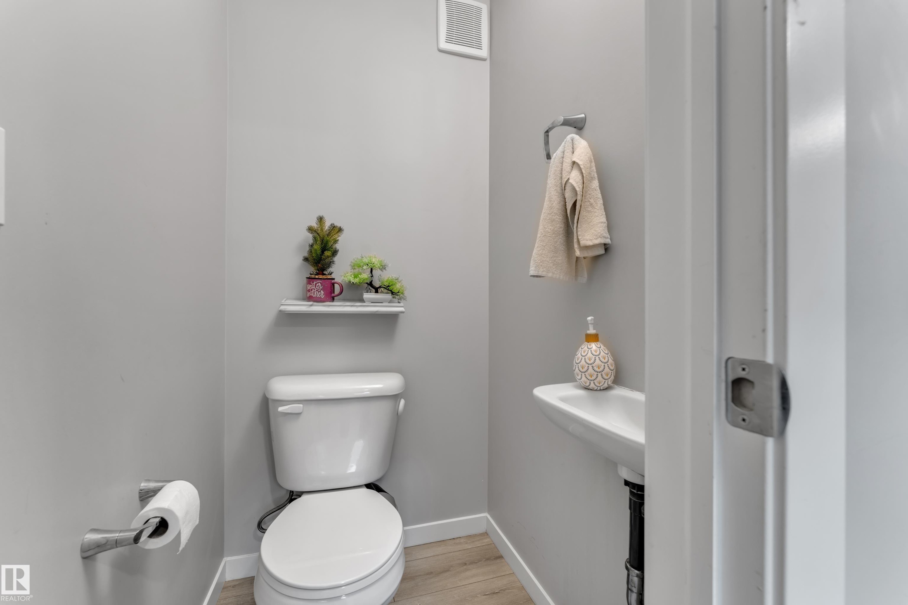 Contemporary powder room featuring a wall-mounted sink, white toilet, and light wood-finish flooring - #82 1816 Rutherford Rd Sw, Edmonton, AB - Indoor Photo Showing Bathroom