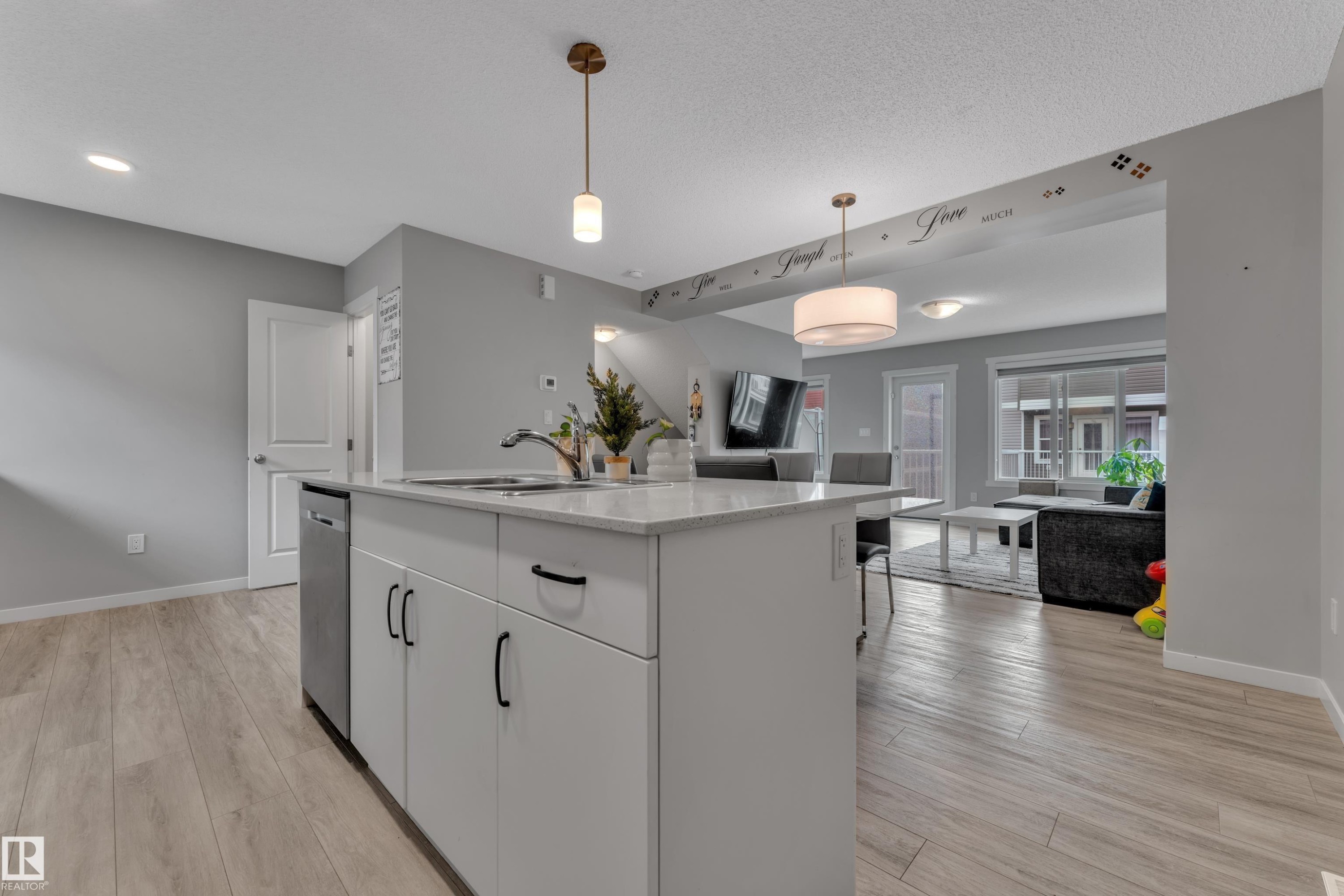 Kitchen island featuring a stainless steel sink, white cabinetry with black hardware, and a light-toned countertop - #82 1816 Rutherford Rd Sw, Edmonton, AB - Indoor