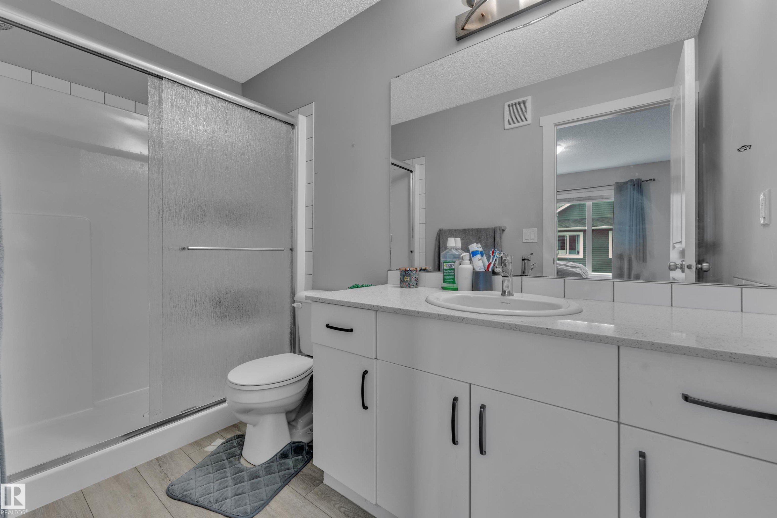 Bathroom featuring a single vanity with an integrated sink, a large mirror, and a shower with frosted sliding doors - #82 1816 Rutherford Rd Sw, Edmonton, AB - Indoor Photo Showing Bathroom