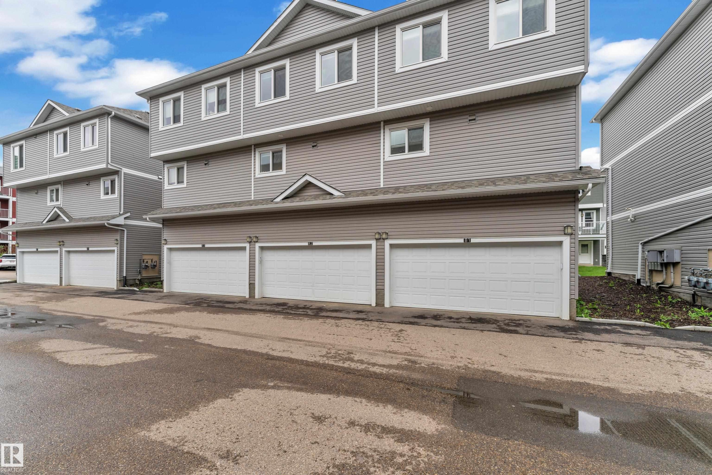 Multi-level residential building featuring gray horizontal siding and individual garage doors - #82 1816 Rutherford Rd Sw, Edmonton, AB - Outdoor With Facade