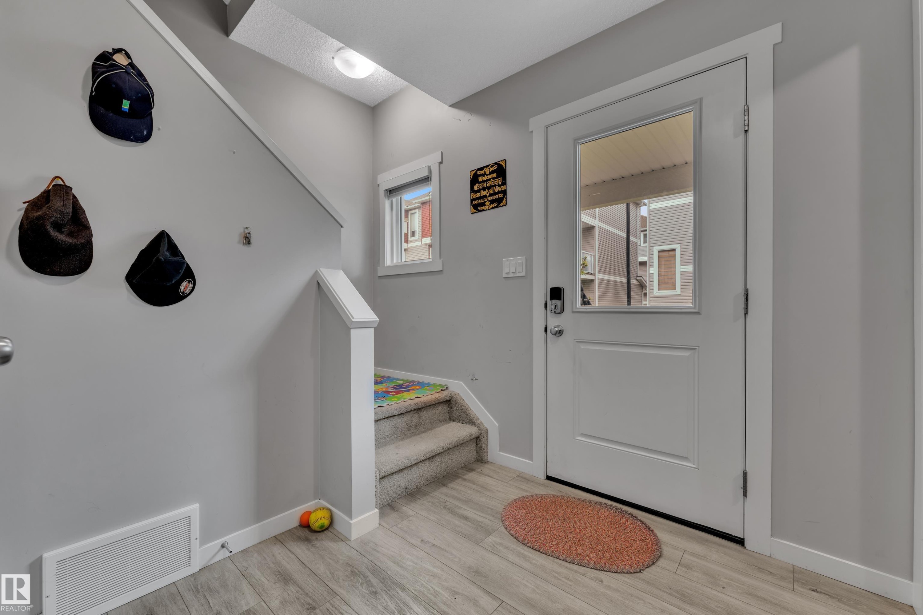 Entryway featuring wood-finish flooring, a white front door with an integrated window, a carpeted staircase with a white railing, and a window with white trim - #82 1816 Rutherford Rd Sw, Edmonton, AB - Indoor Photo Showing Other Room