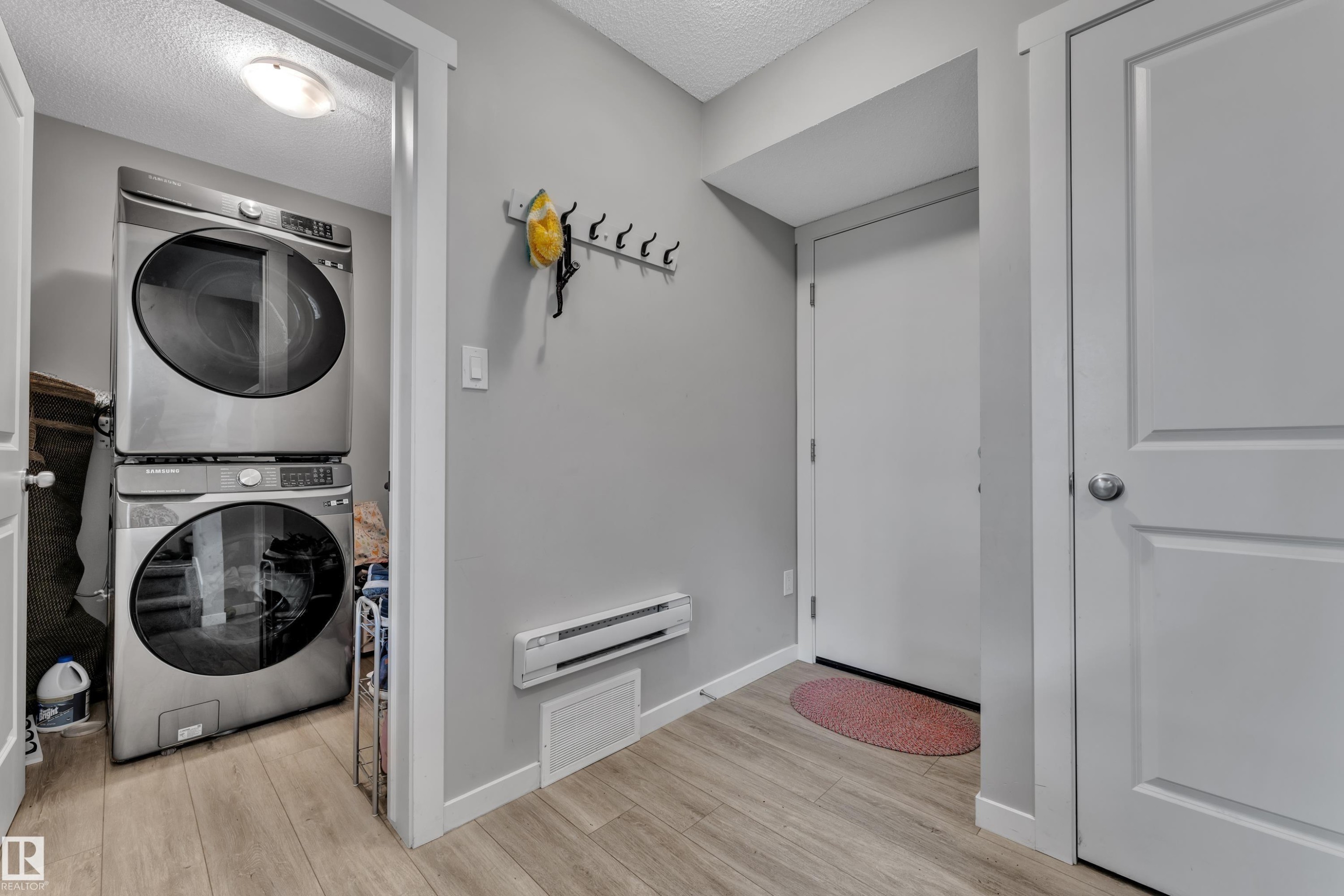 Dedicated laundry area featuring a stacked washer and dryer, light wood-finish flooring, and a wall-mounted coat rack - #82 1816 Rutherford Rd Sw, Edmonton, AB - Indoor Photo Showing Laundry Room