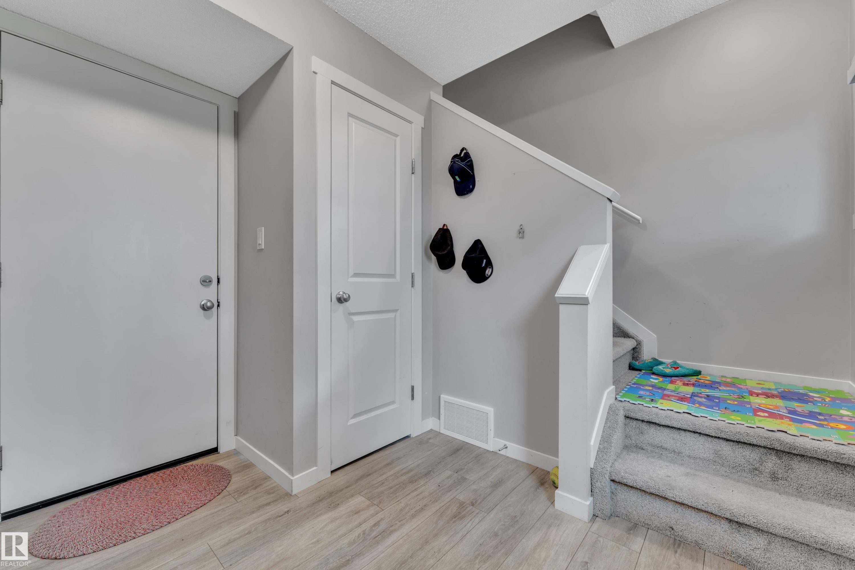 Entryway featuring light wood-finish flooring, light grey painted walls, white trim, and a carpeted staircase with white railings - #82 1816 Rutherford Rd Sw, Edmonton, AB - Indoor