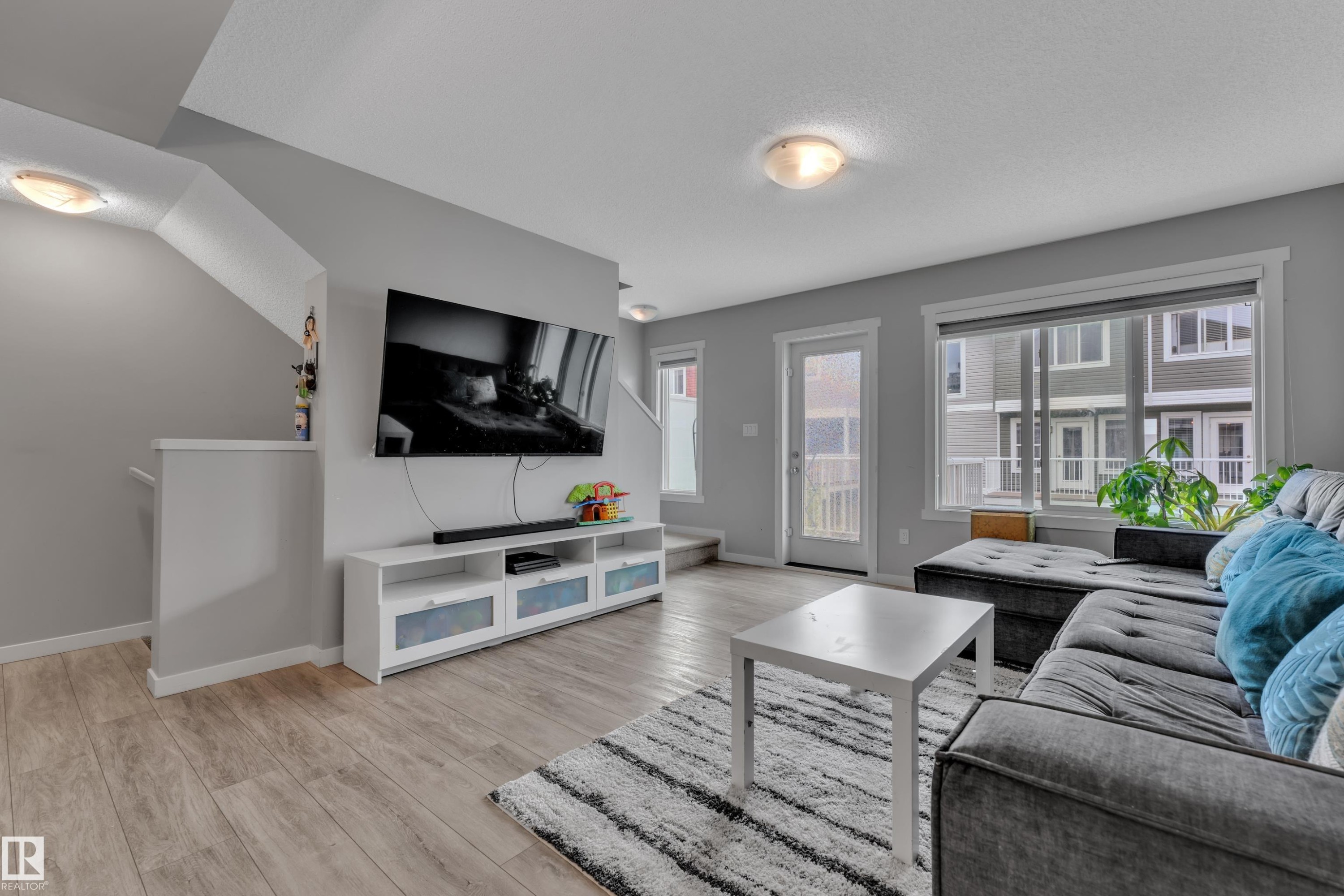 Open-concept living space featuring wood-finish flooring, a contemporary staircase, and multiple windows for natural illumination - #82 1816 Rutherford Rd Sw, Edmonton, AB - Indoor Photo Showing Living Room